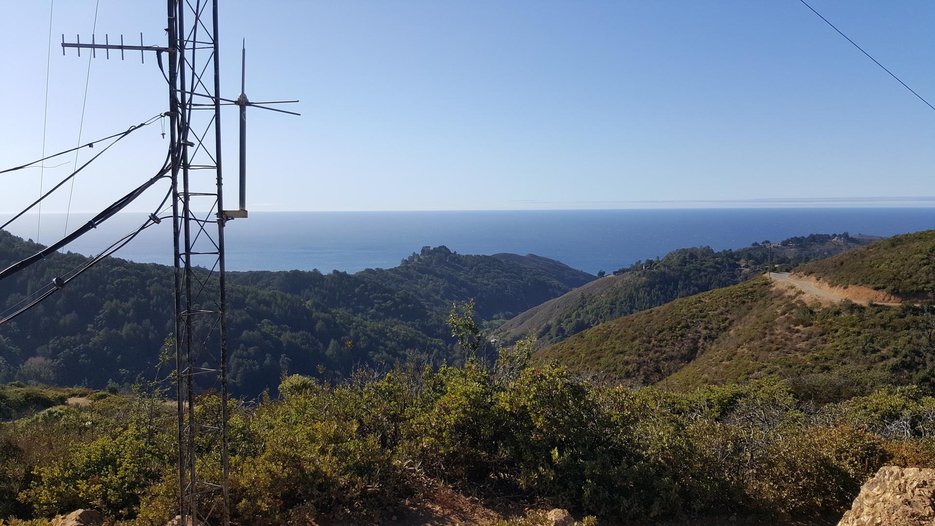 Ocean view over green hills with an antenna in the foreground.