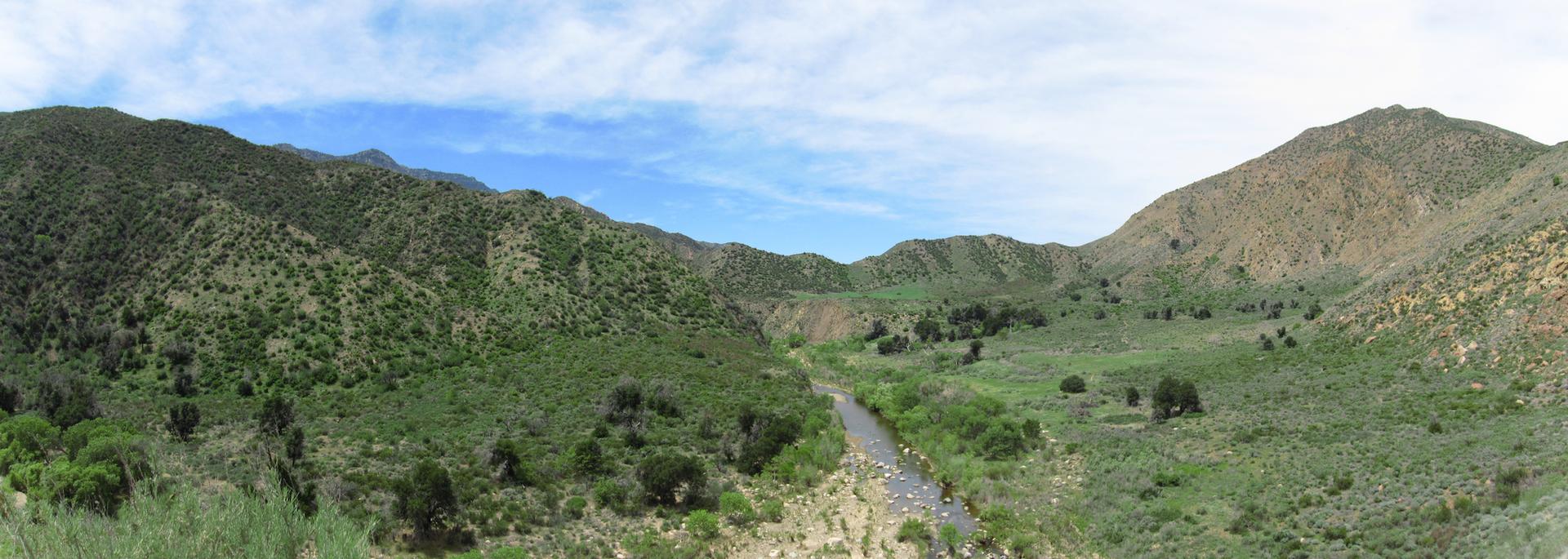 Panoramic view of a green mountain valley with a road under a partly cloudy sky.
