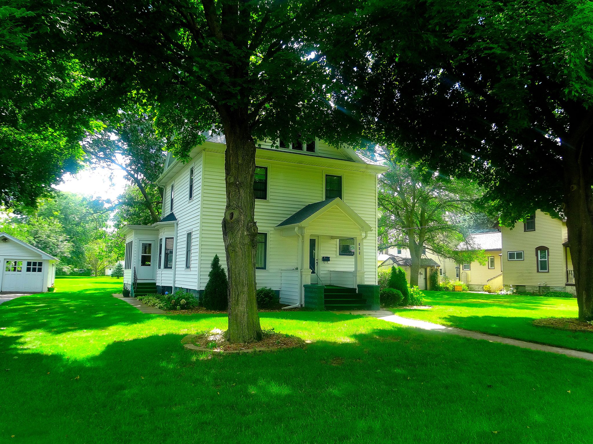 A white house with a green lawn, shaded by large trees on a sunny day. - Great Sauk State Trail