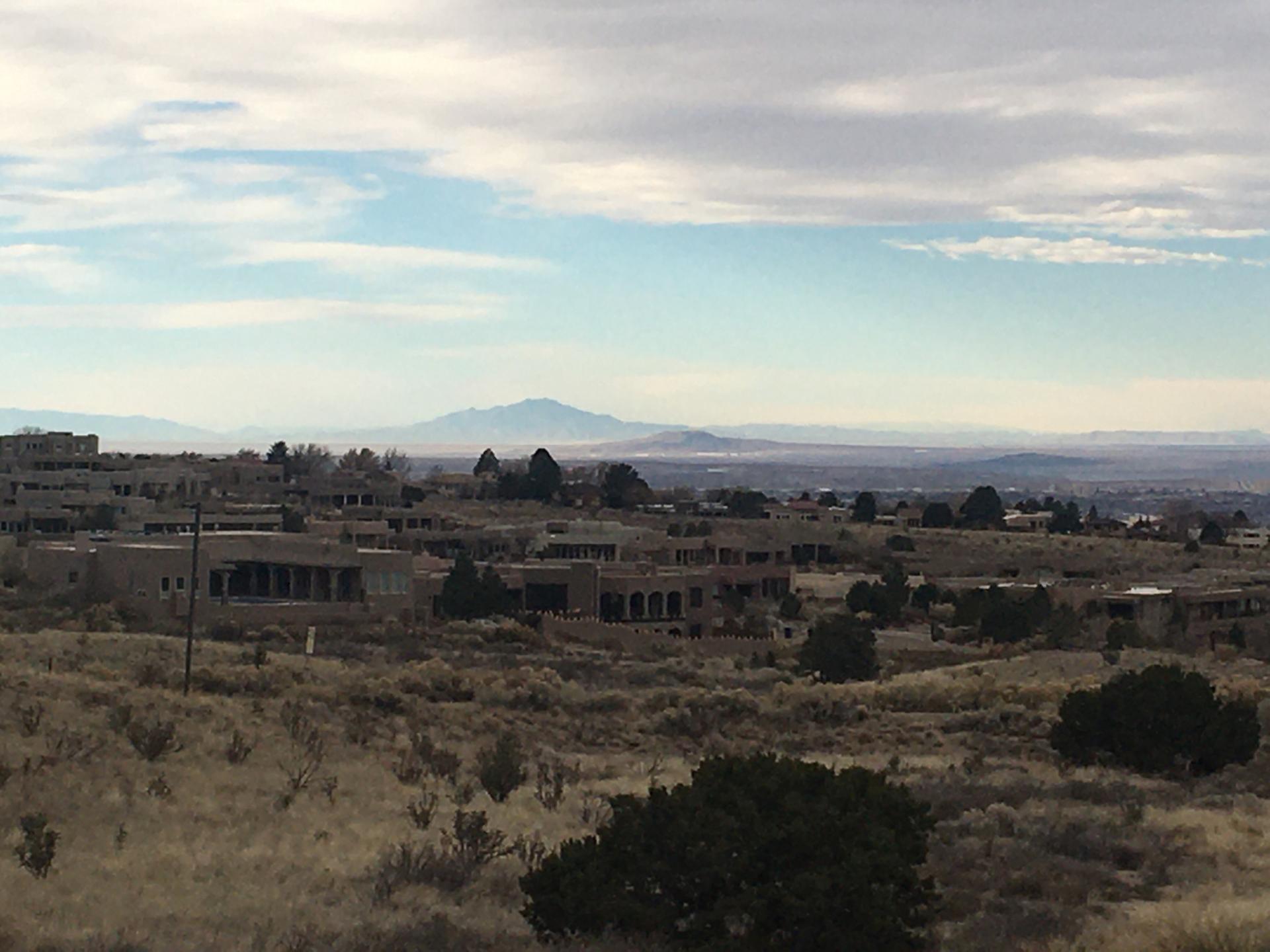 Distant city and mountains under a cloudy sky, dry landscape with buildings.