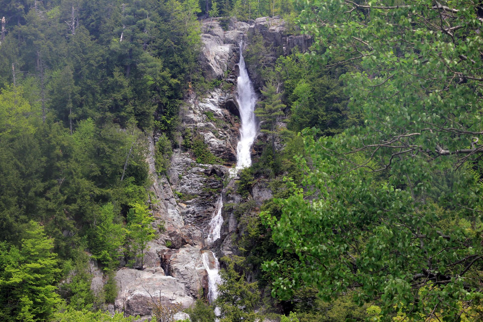 A tall, multi-tiered waterfall cascades down rocky cliffs amidst green forest.