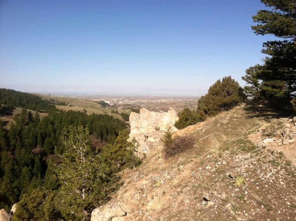 Rocky outcrop on a sunny hillside overlooking a valley and distant town.