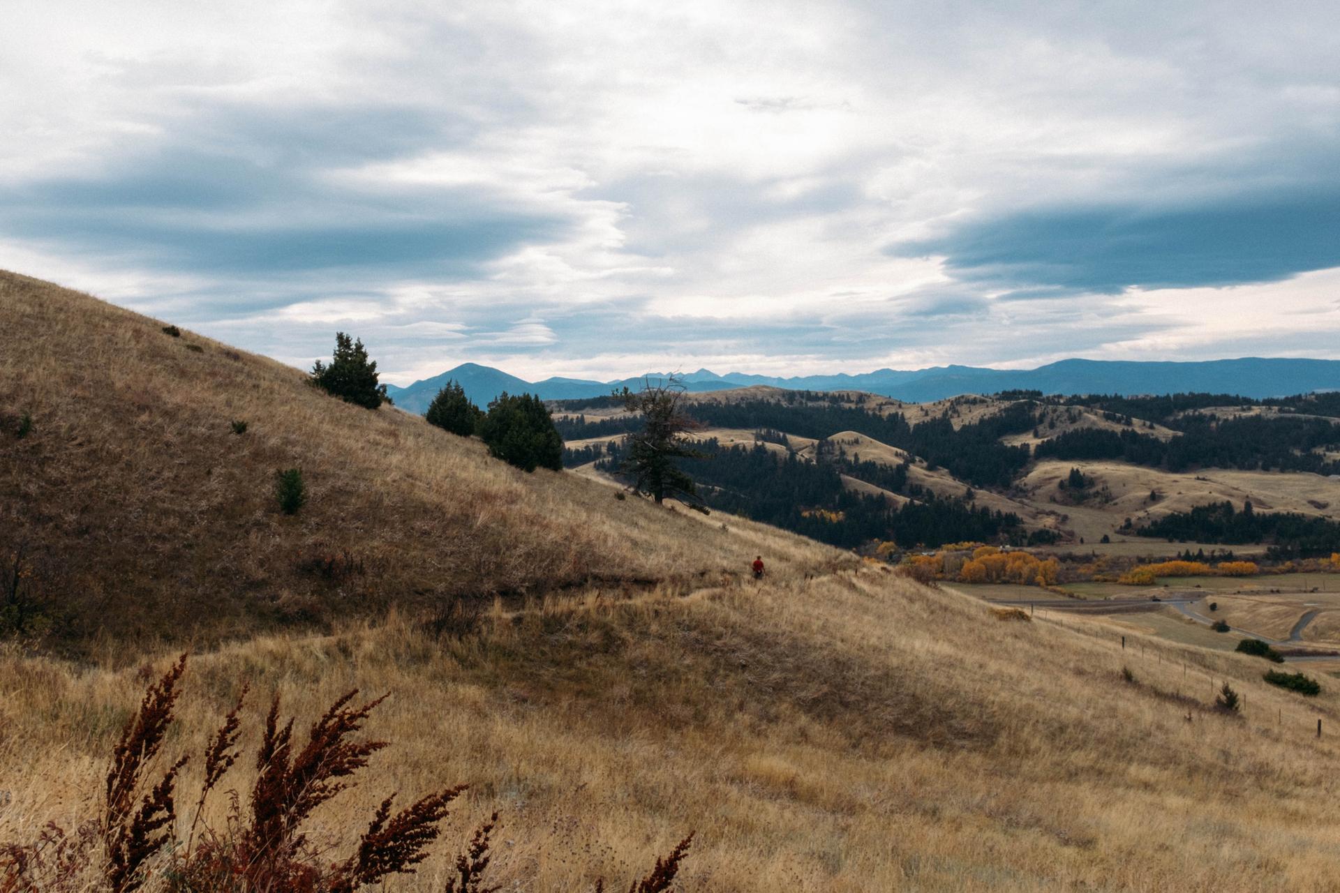 Dry grassy hills and distant mountains under a dramatic cloudy sky.
