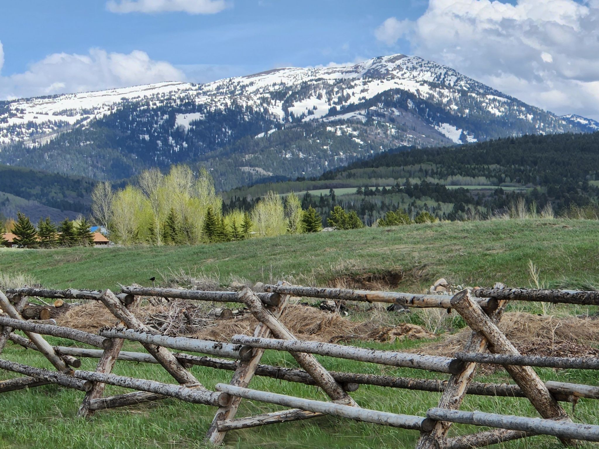 A rustic wooden fence in a grassy field, with snow-dusted mountains beyond. - South Victor Bike Path Loop
