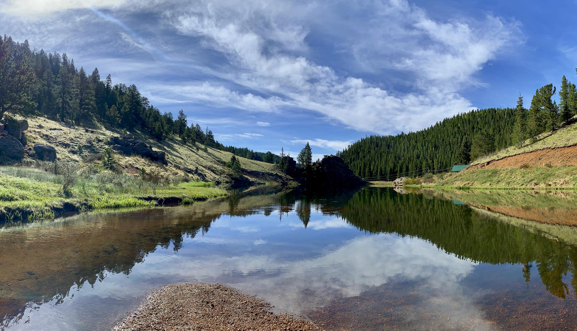 Panoramic view of a calm lake reflecting a blue, cloudy sky.