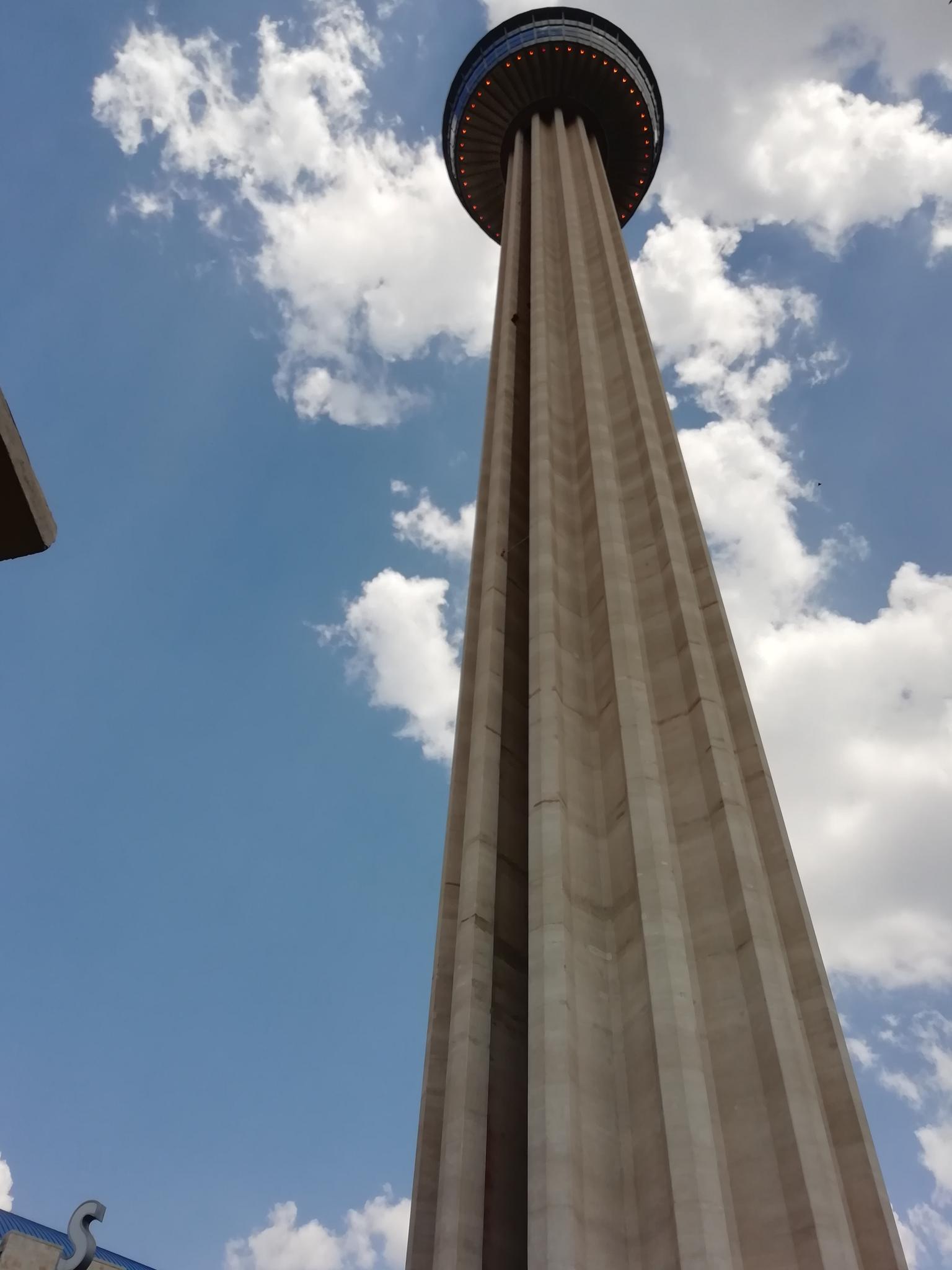 A very tall, slender tower with a circular top against a cloudy blue sky.