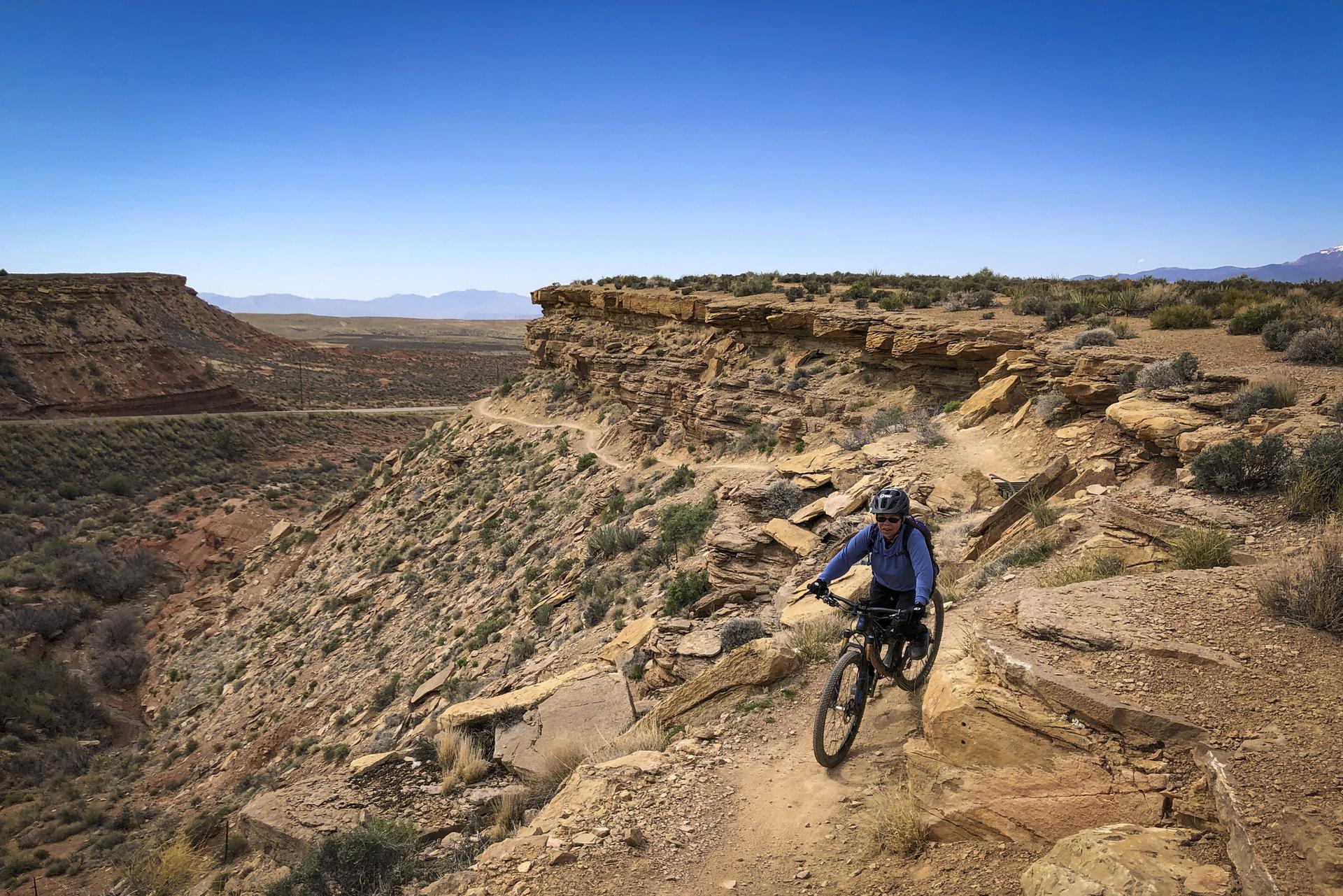 Mountain biker on a rocky cliffside trail under a clear blue sky.