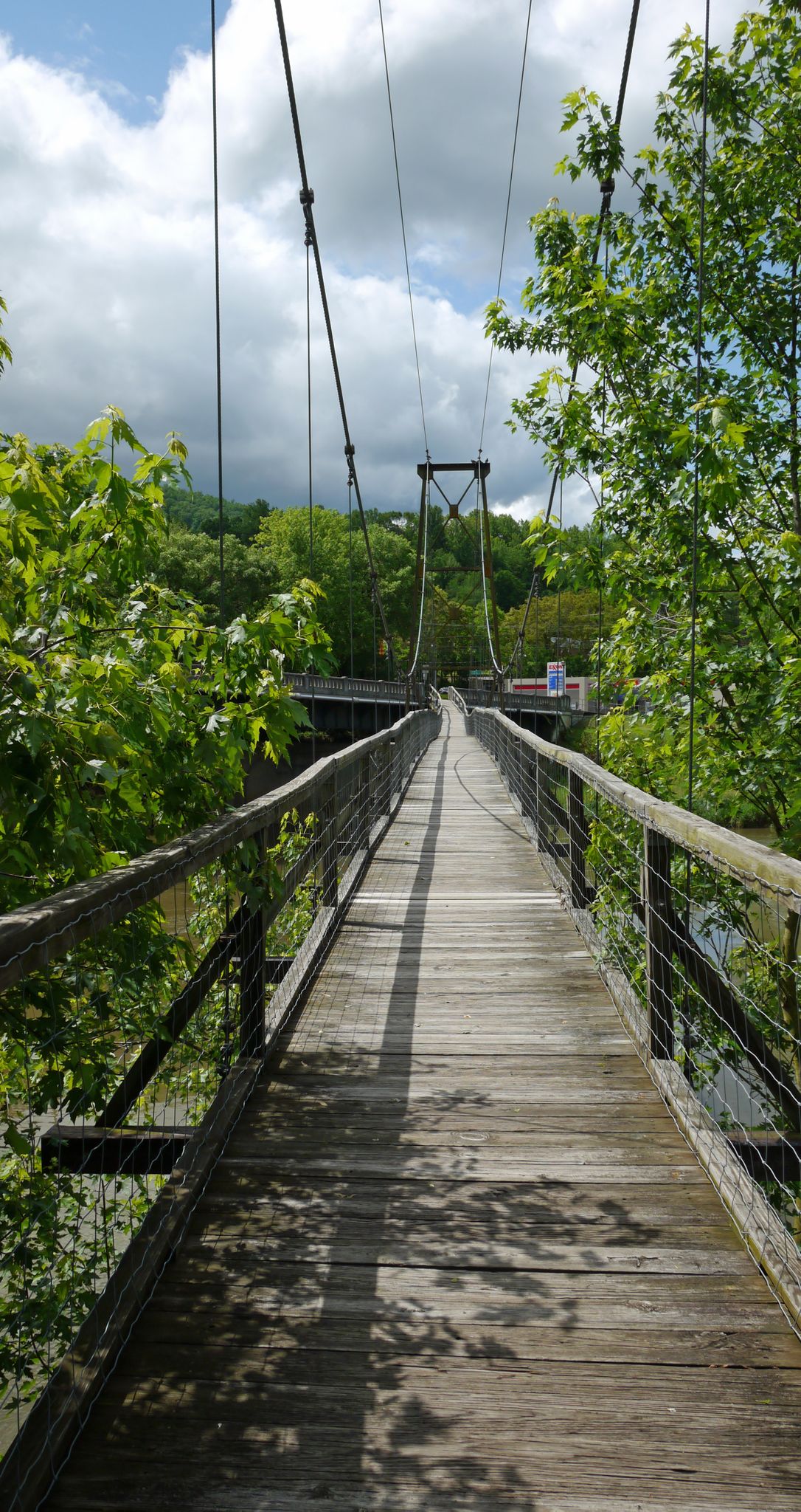 Long wooden suspension bridge over water, surrounded by green trees on a sunny day. - Buchanan Swinging Bridge – Mills Gap Overlook loop from Nace