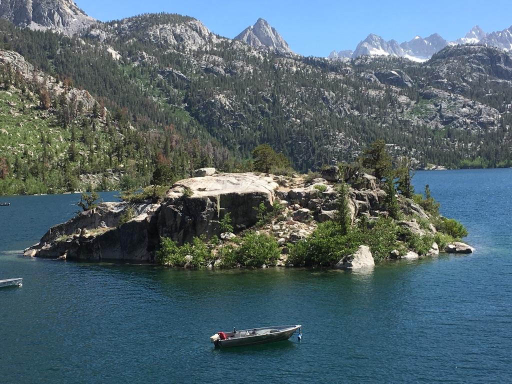 Bright day, a small boat near a rocky island in a large lake.