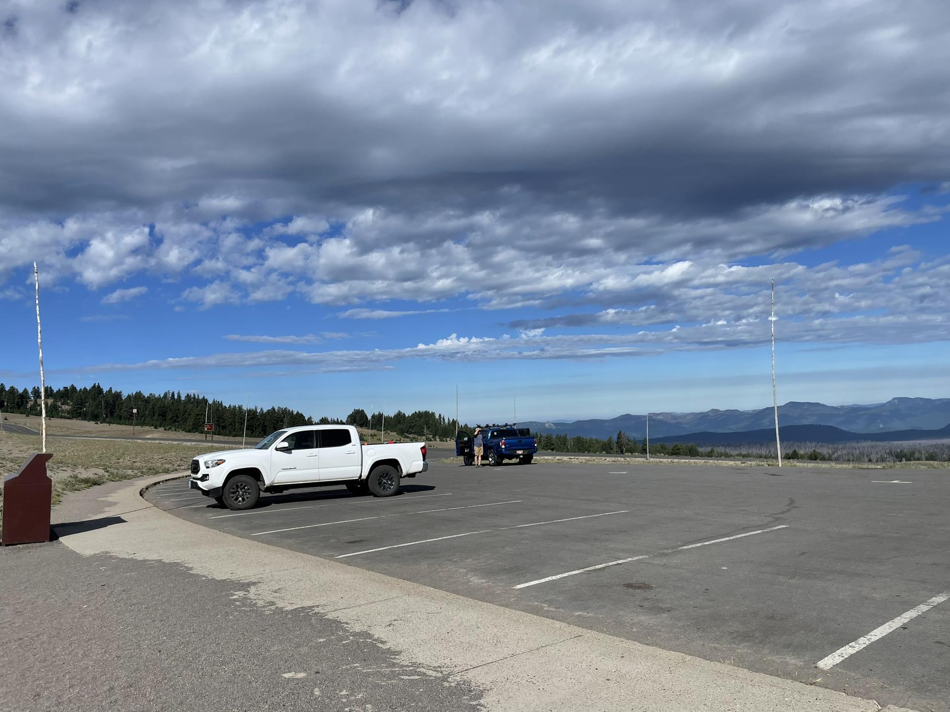 Two trucks parked in a lot with distant mountains under a cloudy sky.