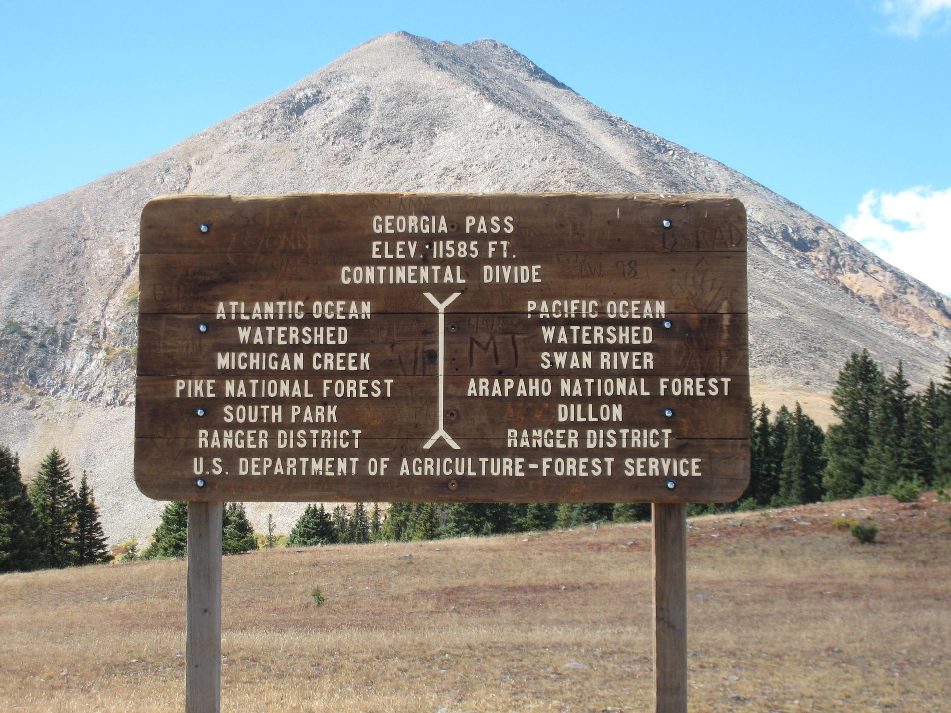 A wooden sign stands before a large, barren mountain peak.