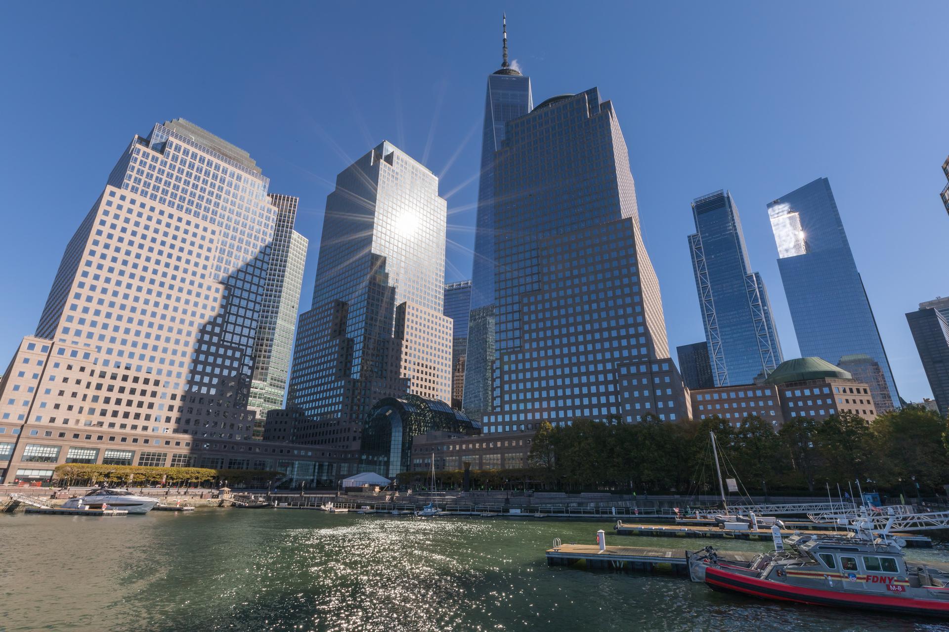 Tall city buildings reflecting bright sun over a waterfront with boats.