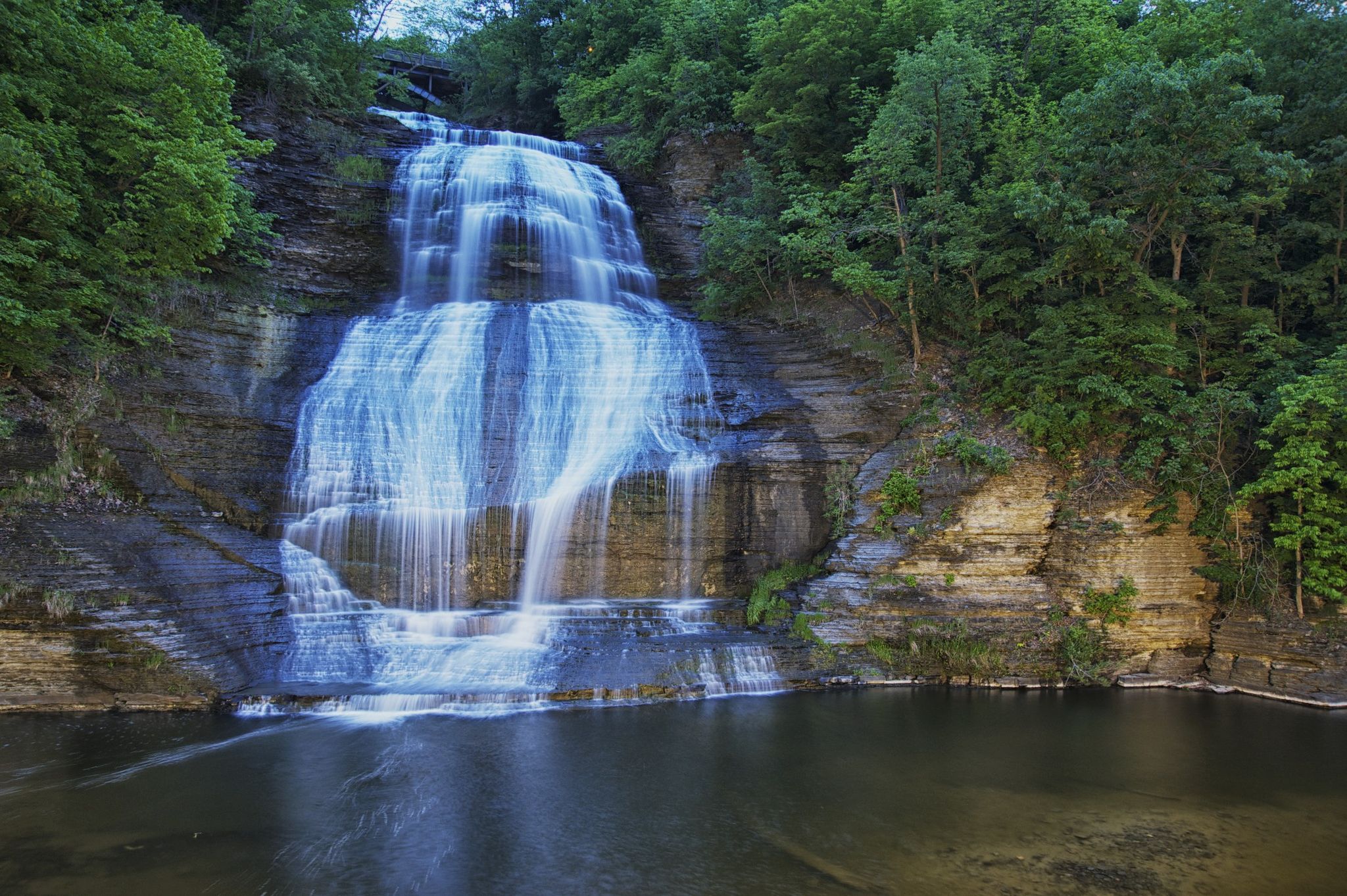 Wide waterfall cascades into a dark pool, surrounded by lush green forest. - Shequaga Falls Park – Mural of Catharine Montour loop from Shequaga Falls