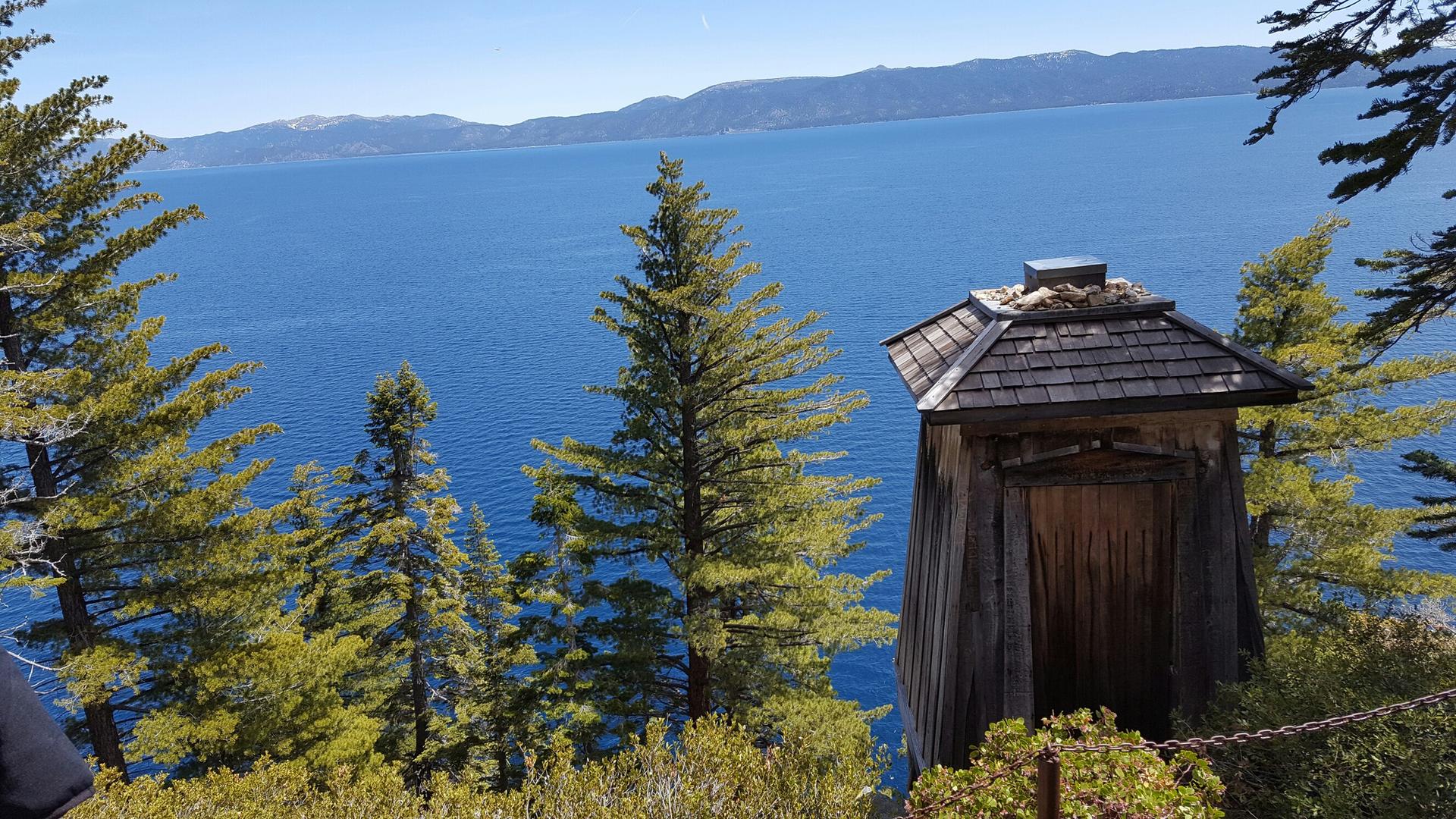 Small wooden structure overlooking a vast blue lake and distant mountains.