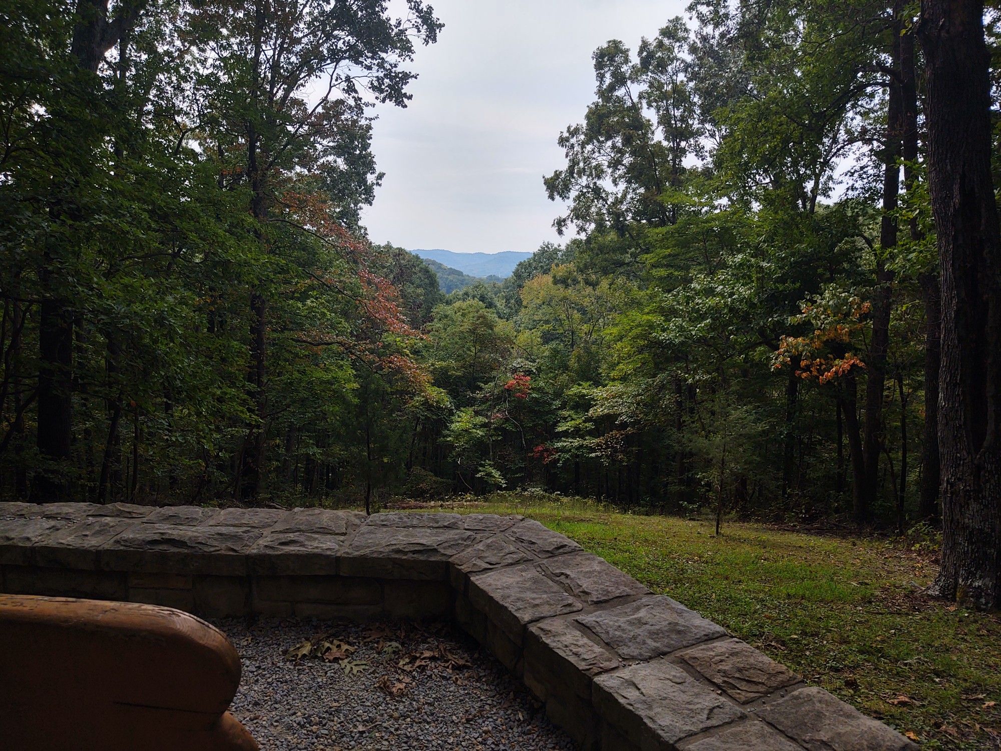 Stone wall overlooking a forest clearing with distant mountains under cloudy sky. - View of Percy Warner Park – Percy Warner Park loop from Belle Meade