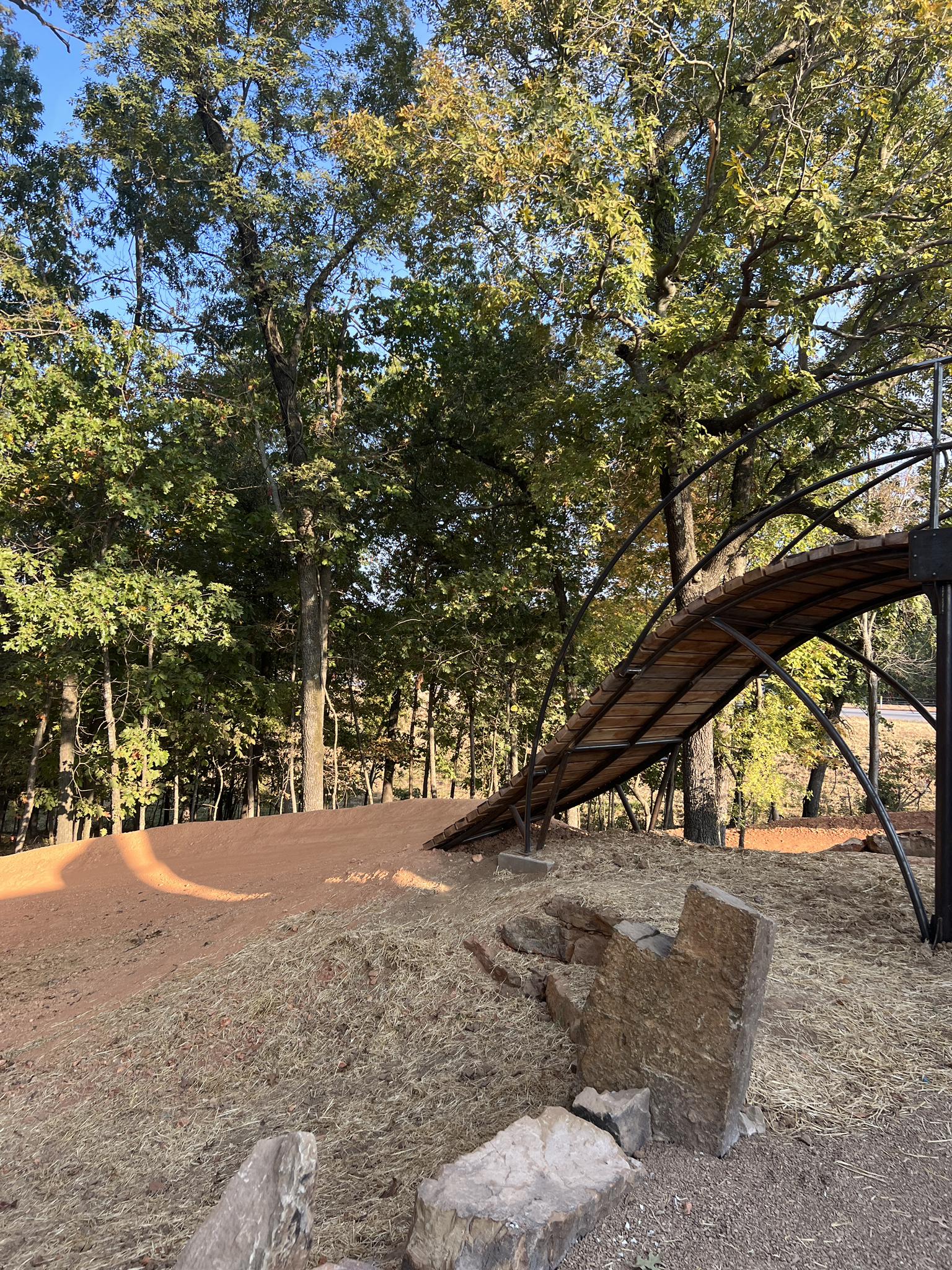 Elevated wooden bike bridge curving through green trees on a sunny day.