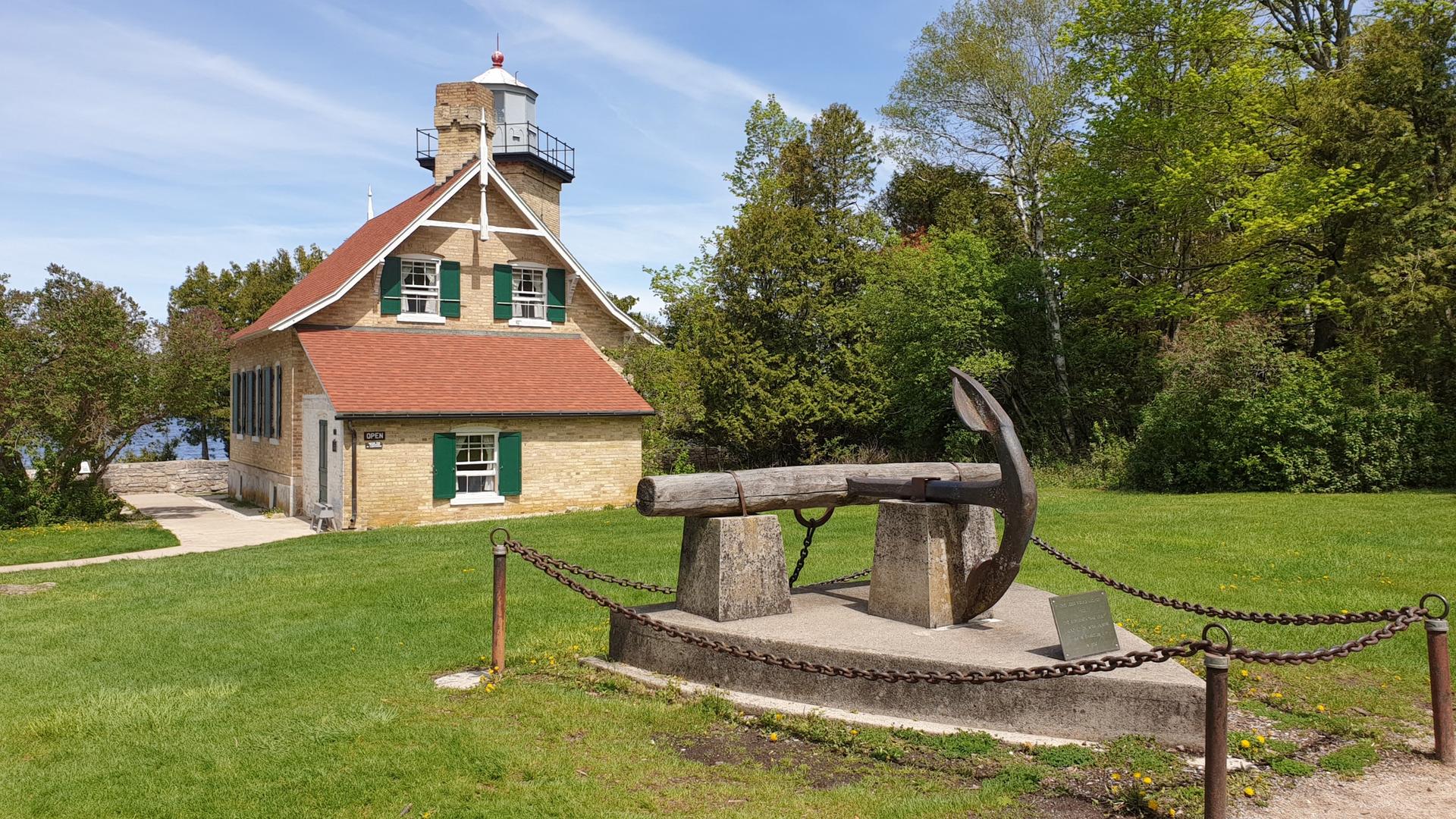 Brick lighthouse with an anchor monument on a sunny green lawn.