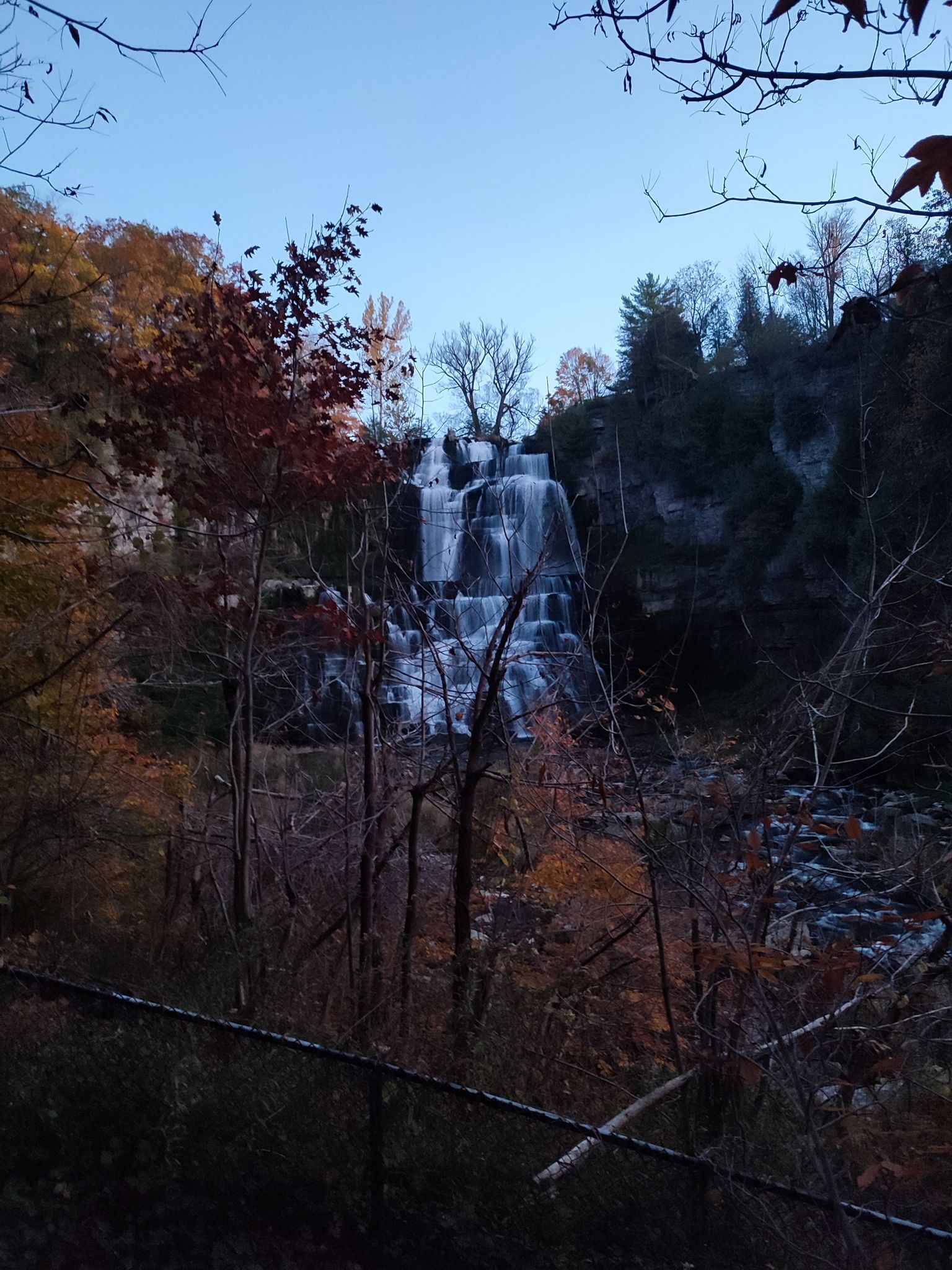 Multi-tiered waterfall in a dark, forested gorge with autumn trees at twilight. - Gorge Trail