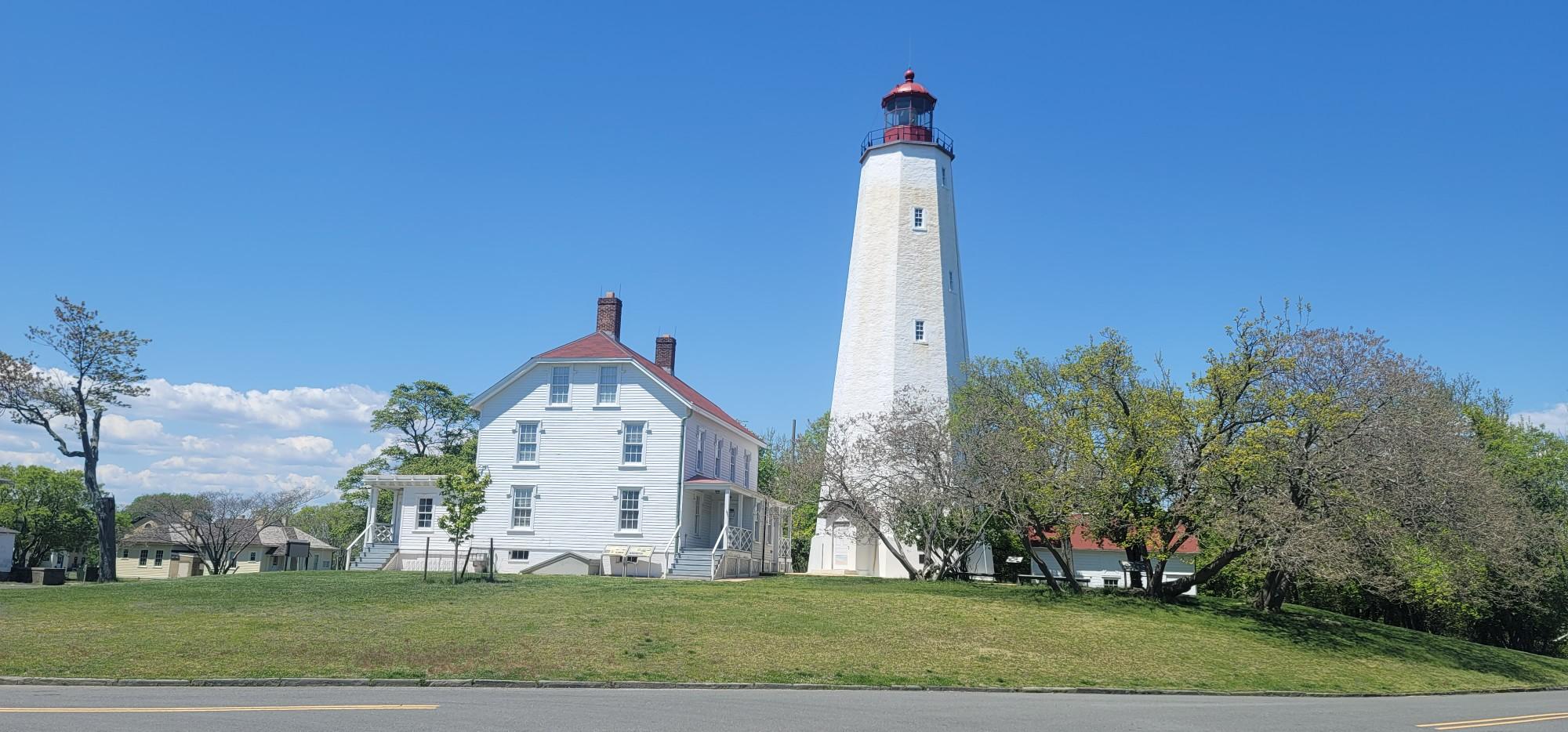 A tall white lighthouse and a house on a green hill, clear sky.