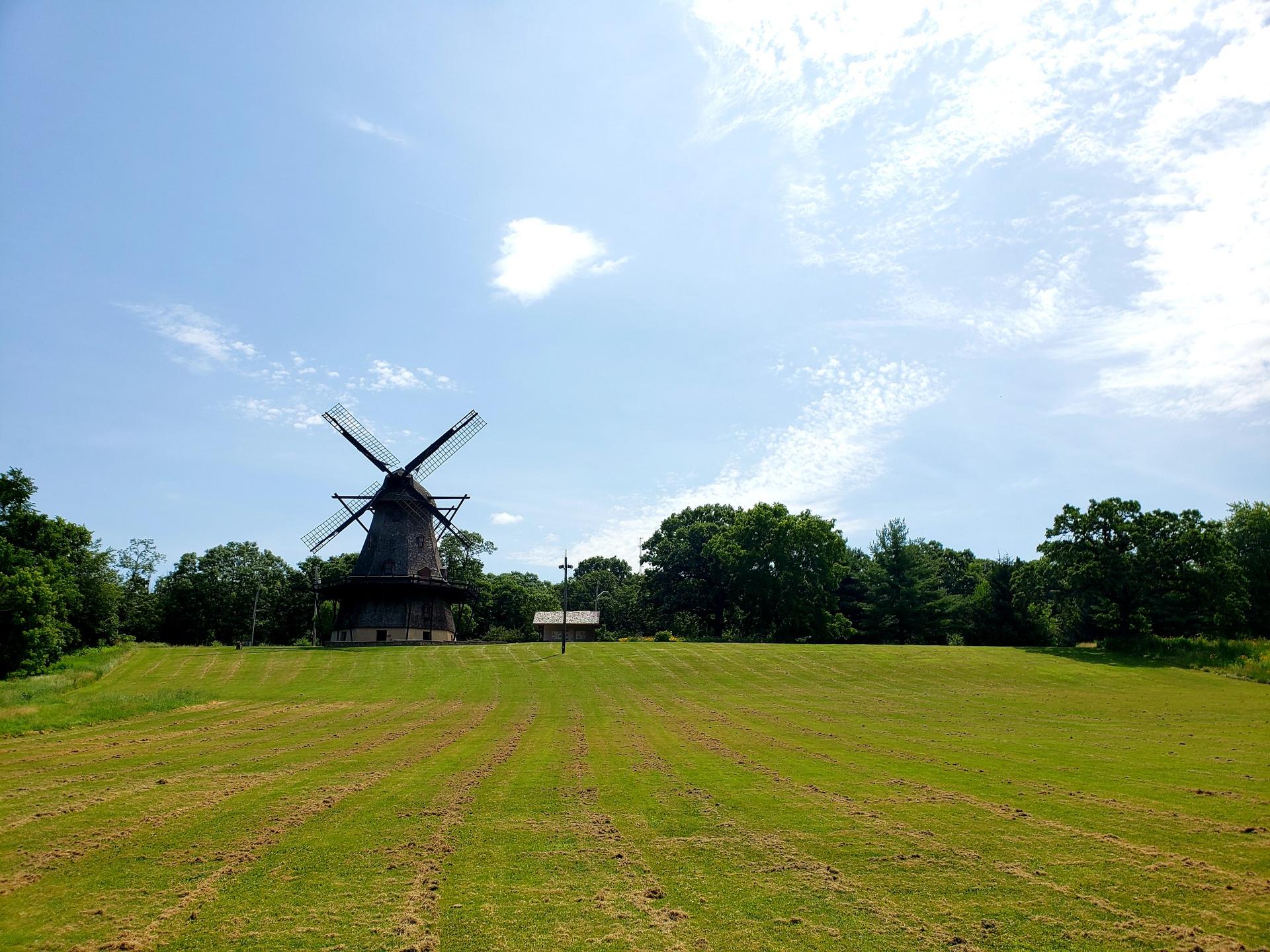 A large windmill stands in a green field under a bright blue sky.