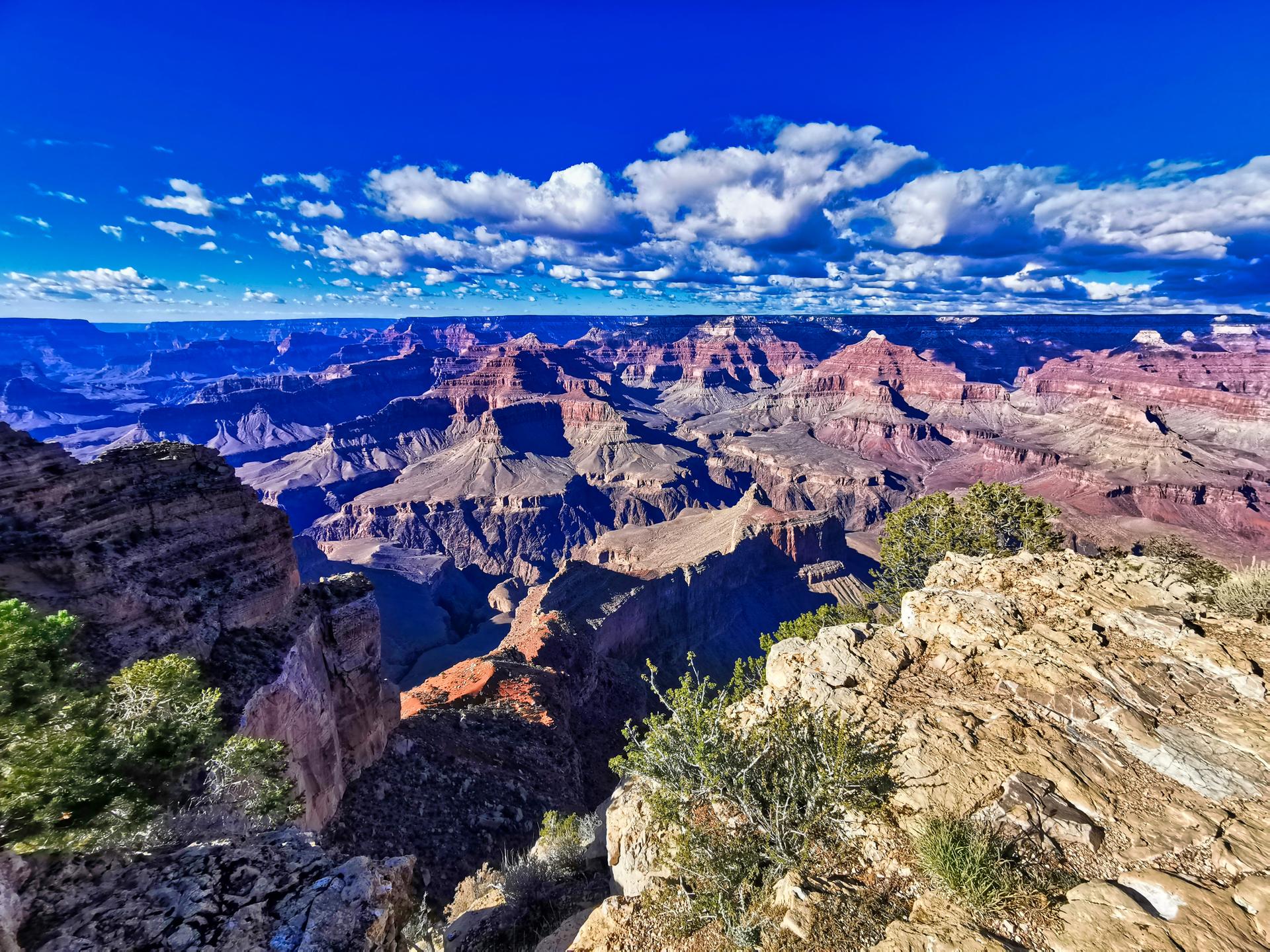 Vast, sunlit canyon with layered rock formations under a bright blue sky.