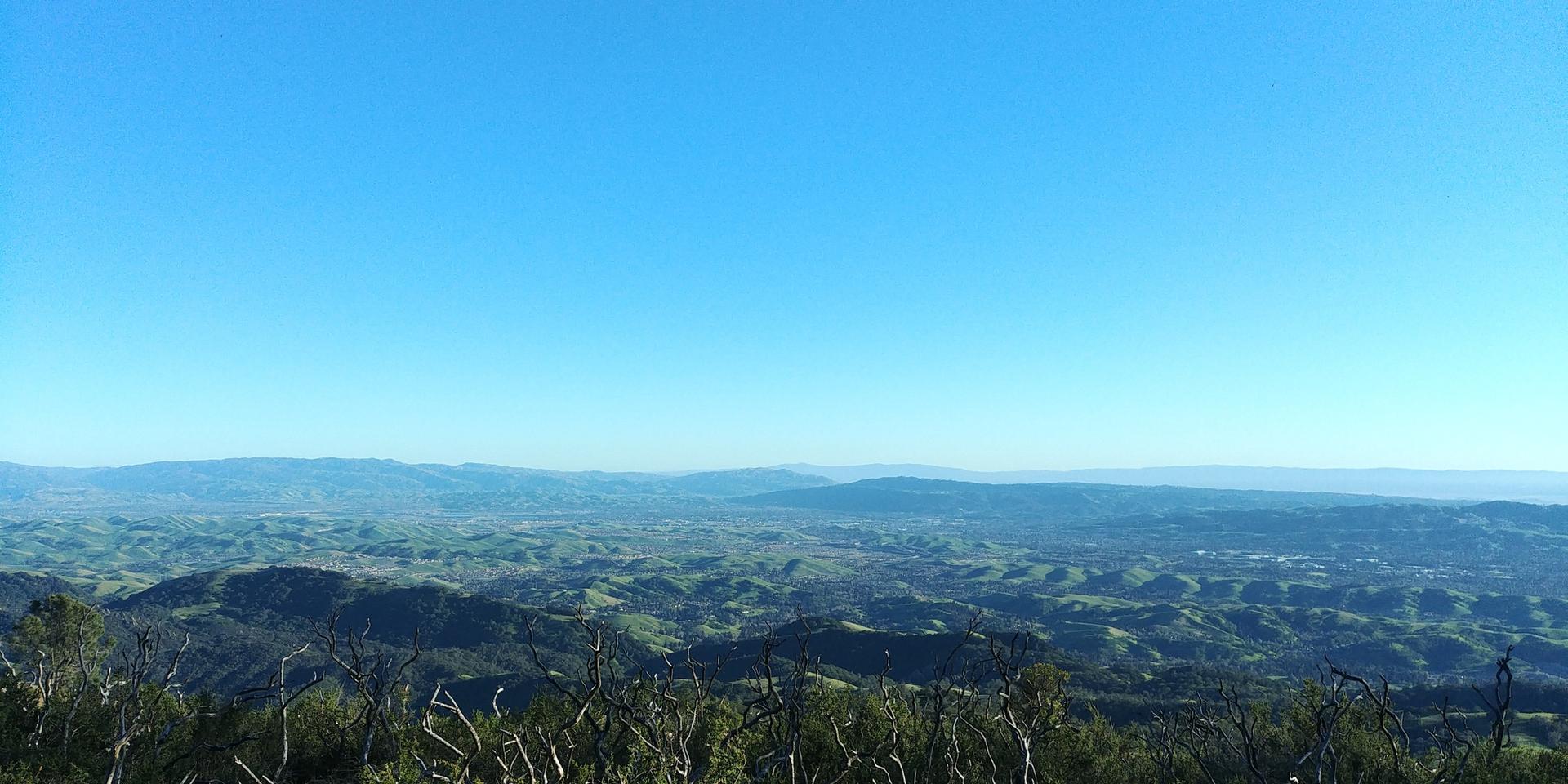 A vast landscape of green hills and distant plains under a bright blue sky.