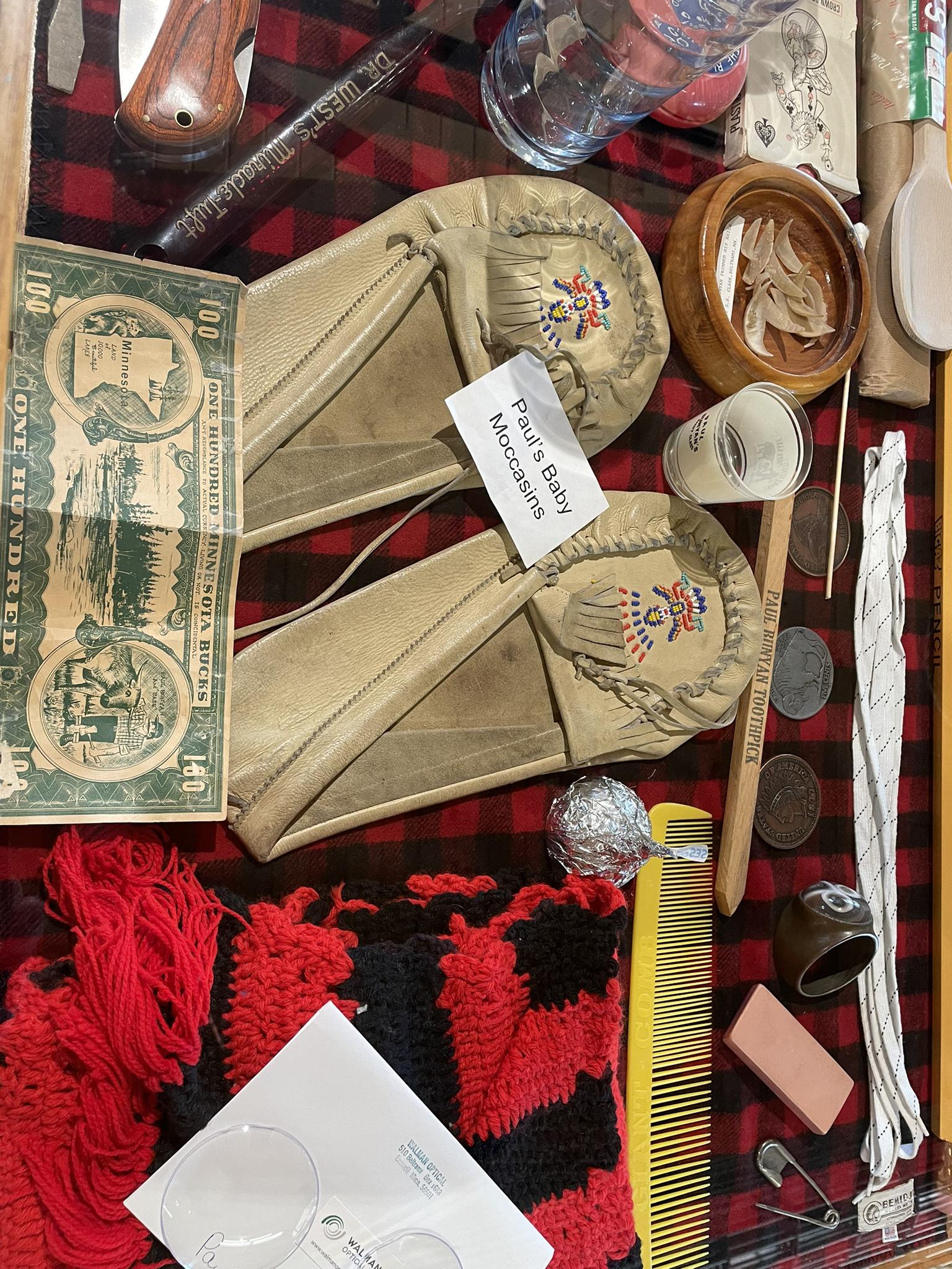 A collection of historical items, including moccasins and old money, on a plaid blanket.