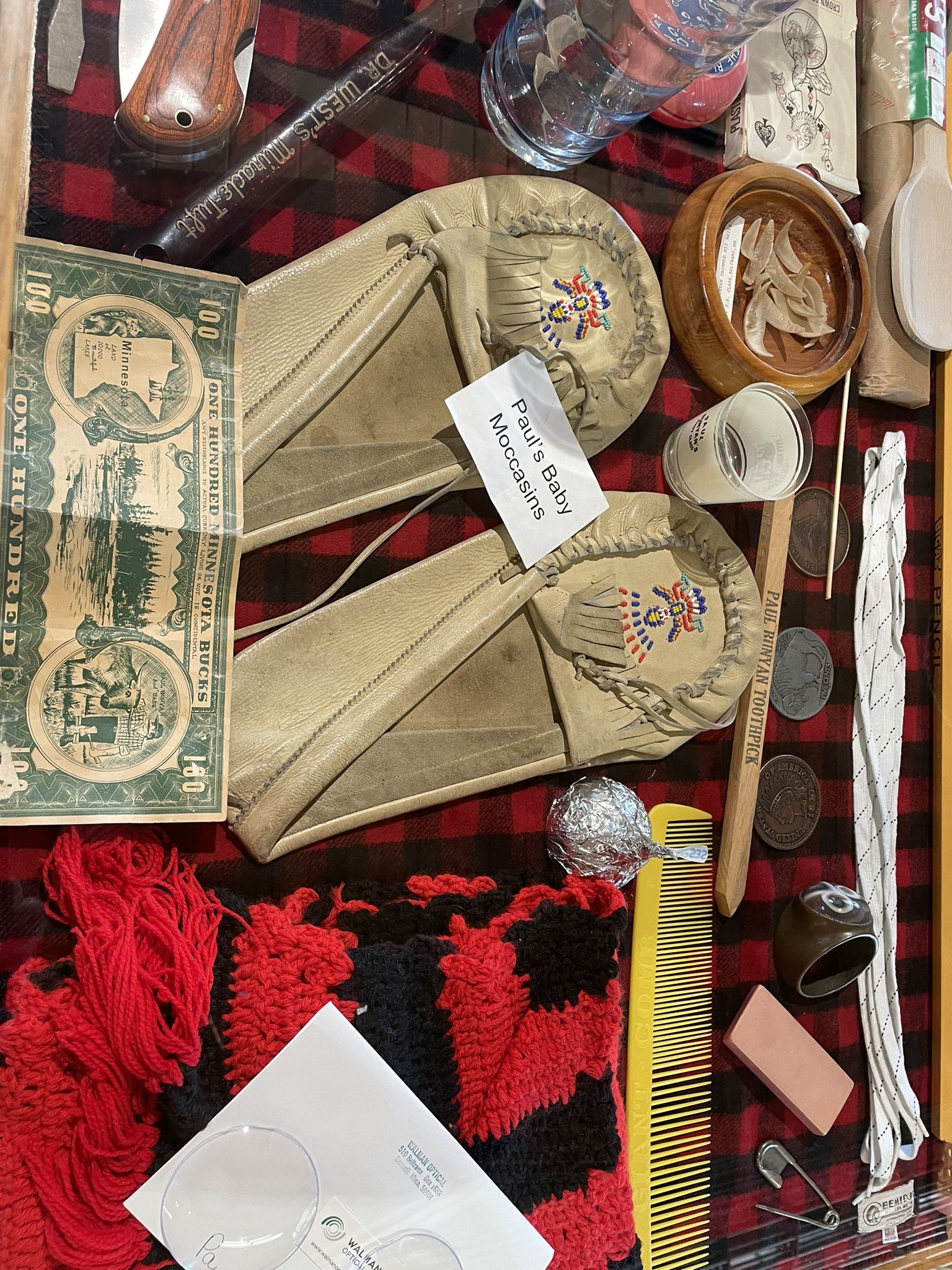 A collection of historical items, including moccasins and old money, on a plaid blanket. - Hiking loop from Bemidji