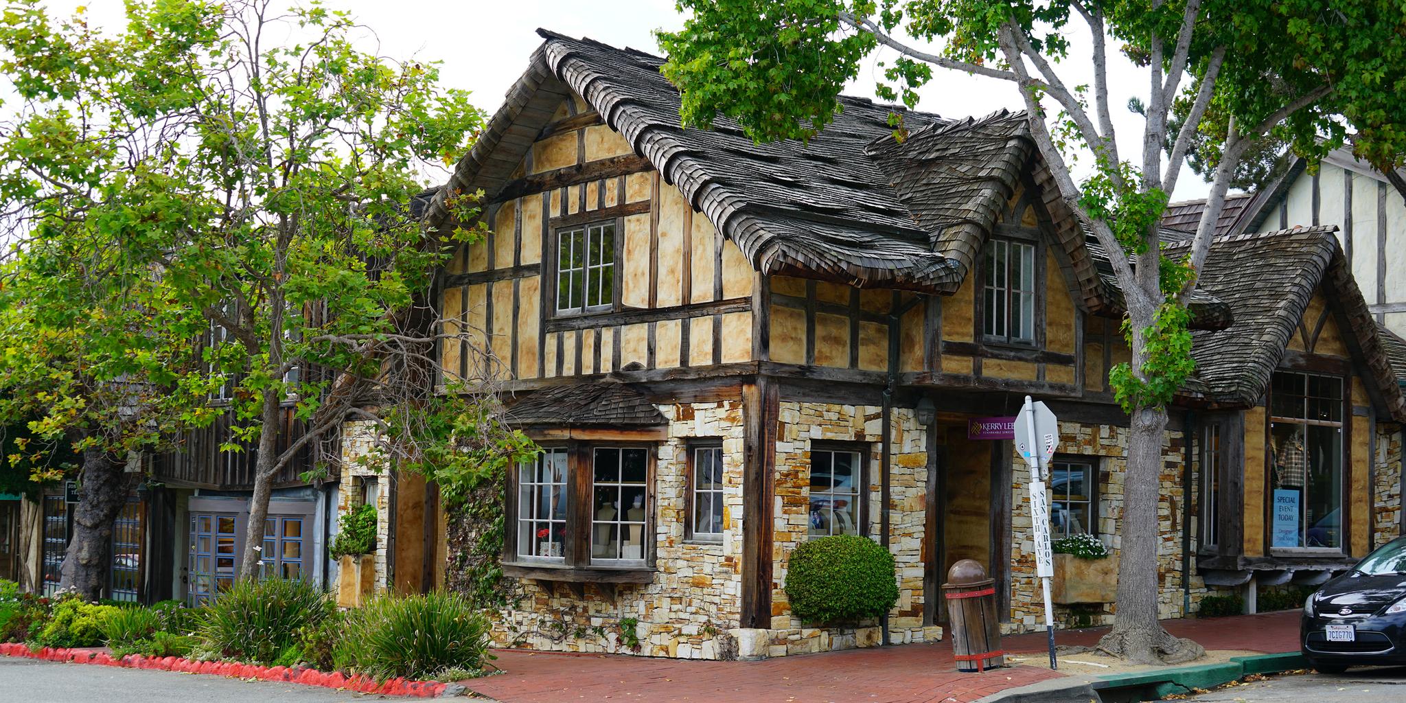 Quaint stone and timber house with a shingled roof, surrounded by trees.