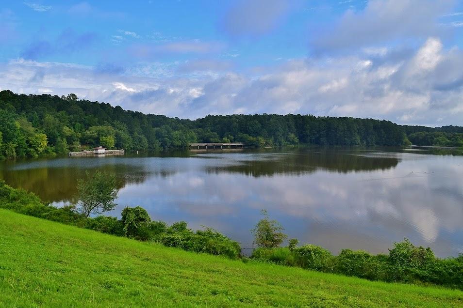 A large, calm lake reflects clouds, surrounded by green hills and forest.