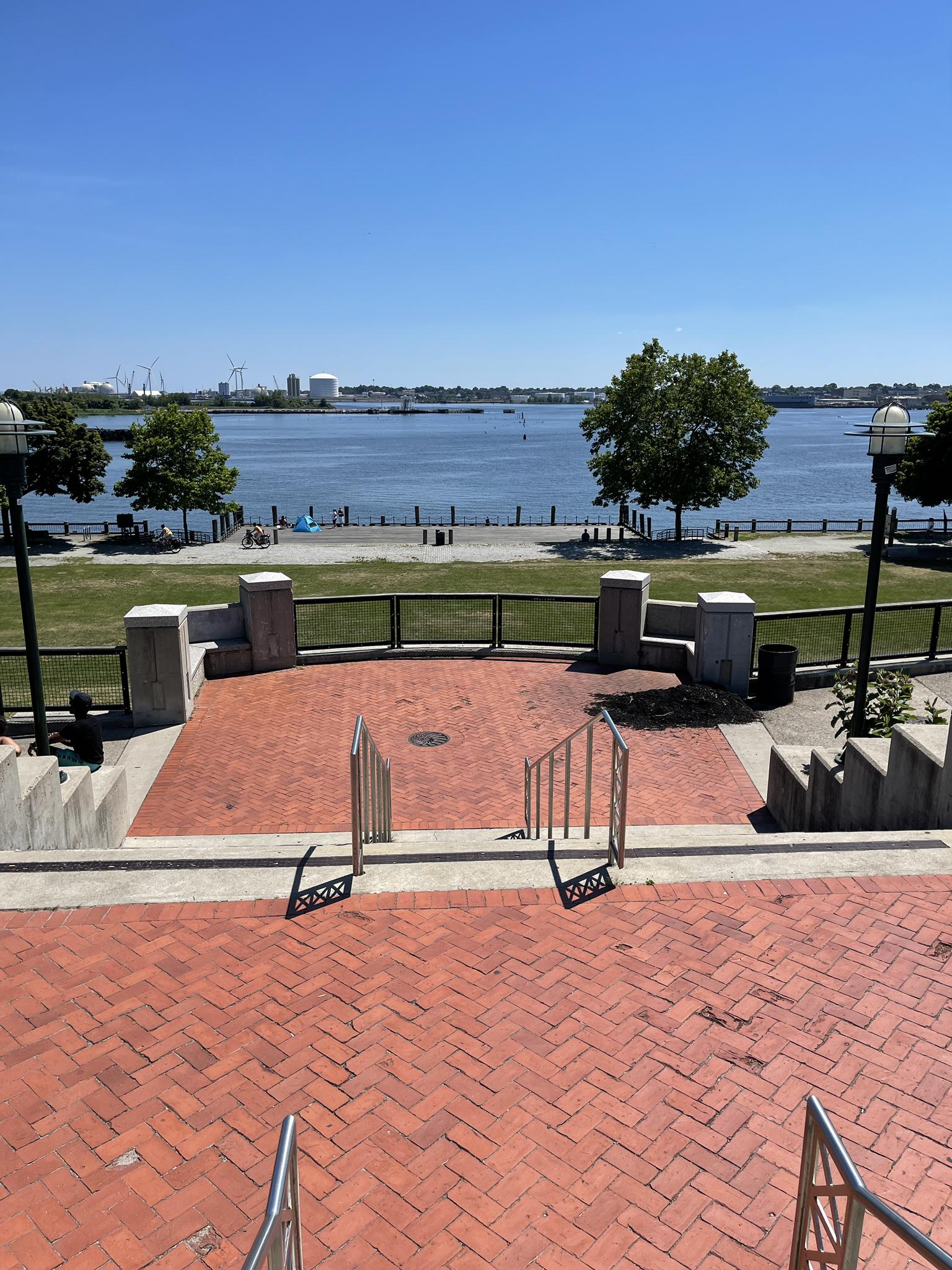 Brick patio overlooking a sunny waterfront with distant people and trees.