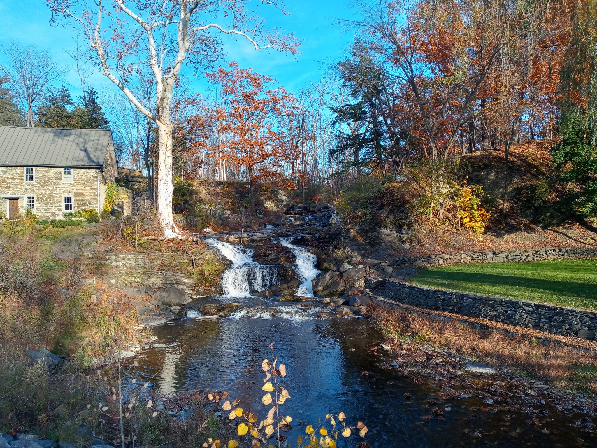 Waterfall cascading past an old stone building and autumn trees. - Albany-Hudson Electric Trail – Claverack Creek Waterfall loop from Lorenz Park