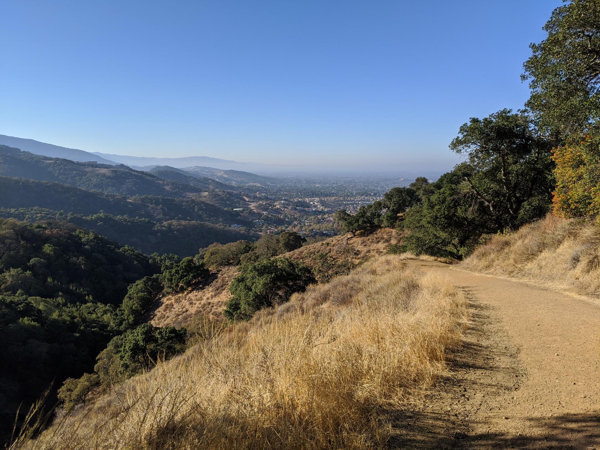 Dirt path on a hillside overlooking a hazy valley and distant mountains.