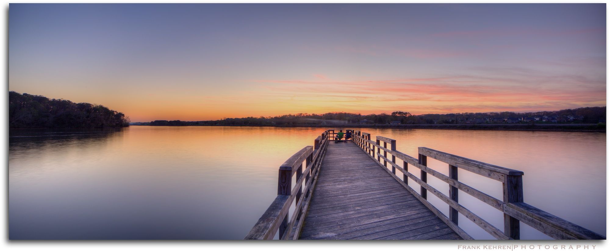Long wooden pier extending into calm water at sunset with two people. - Golf Loop