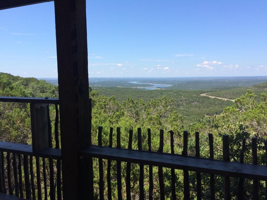 View from a wooden balcony over a vast green forest and distant lake.