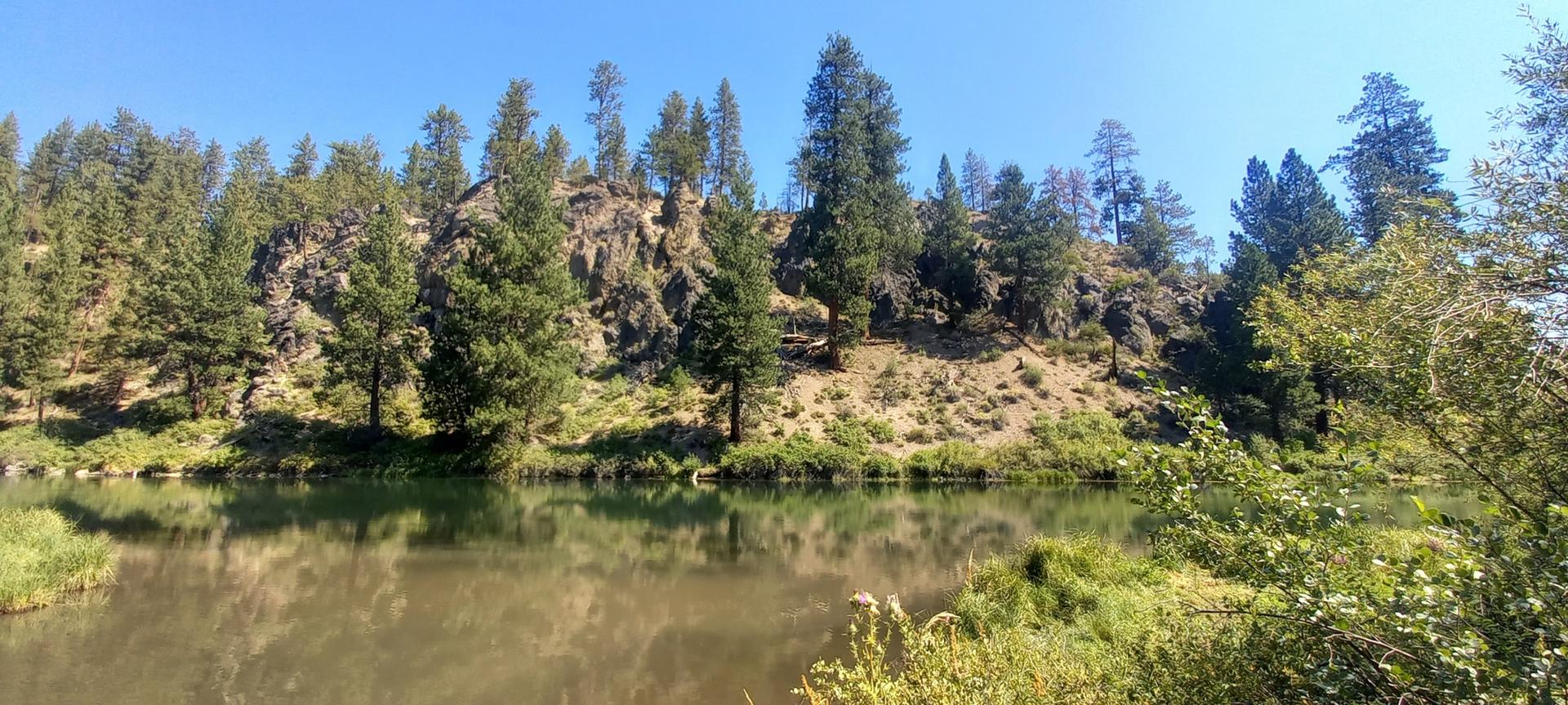 Panoramic view of a calm river reflecting trees and rocky hills.