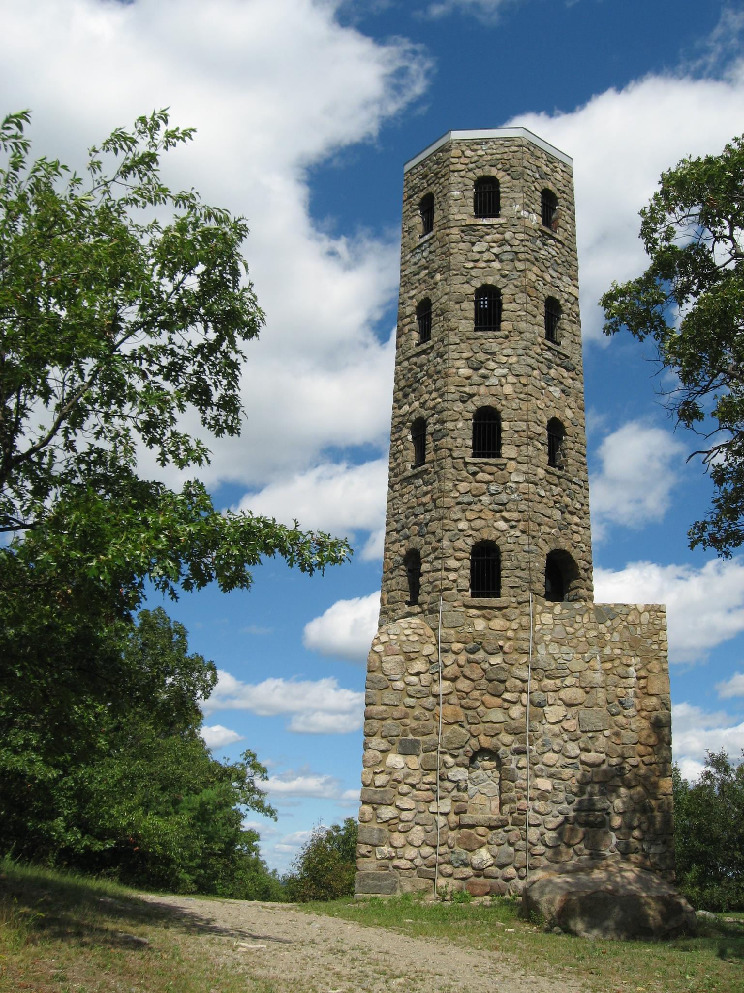 A tall, octagonal stone tower stands against a bright blue, cloudy sky.