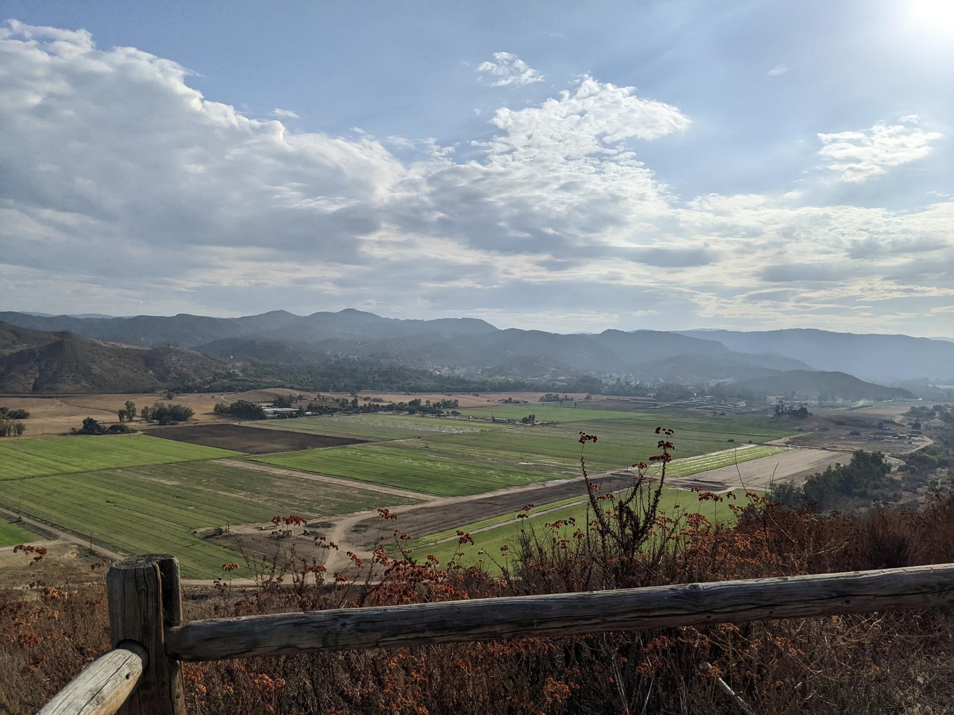 Panoramic view of green agricultural fields and distant mountains under a cloudy sky.