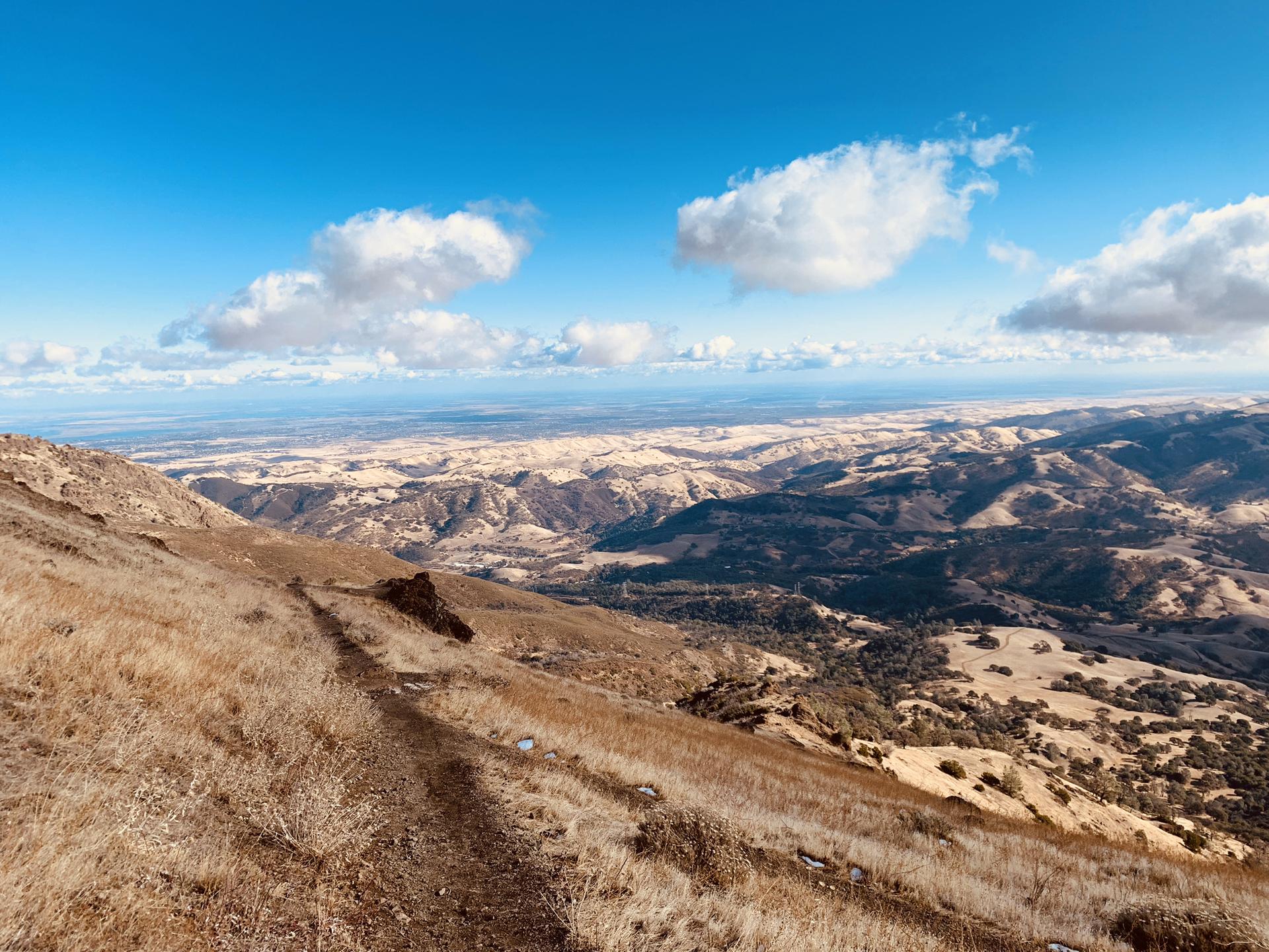 Expansive view of dry, rolling hills under a partly cloudy sky.