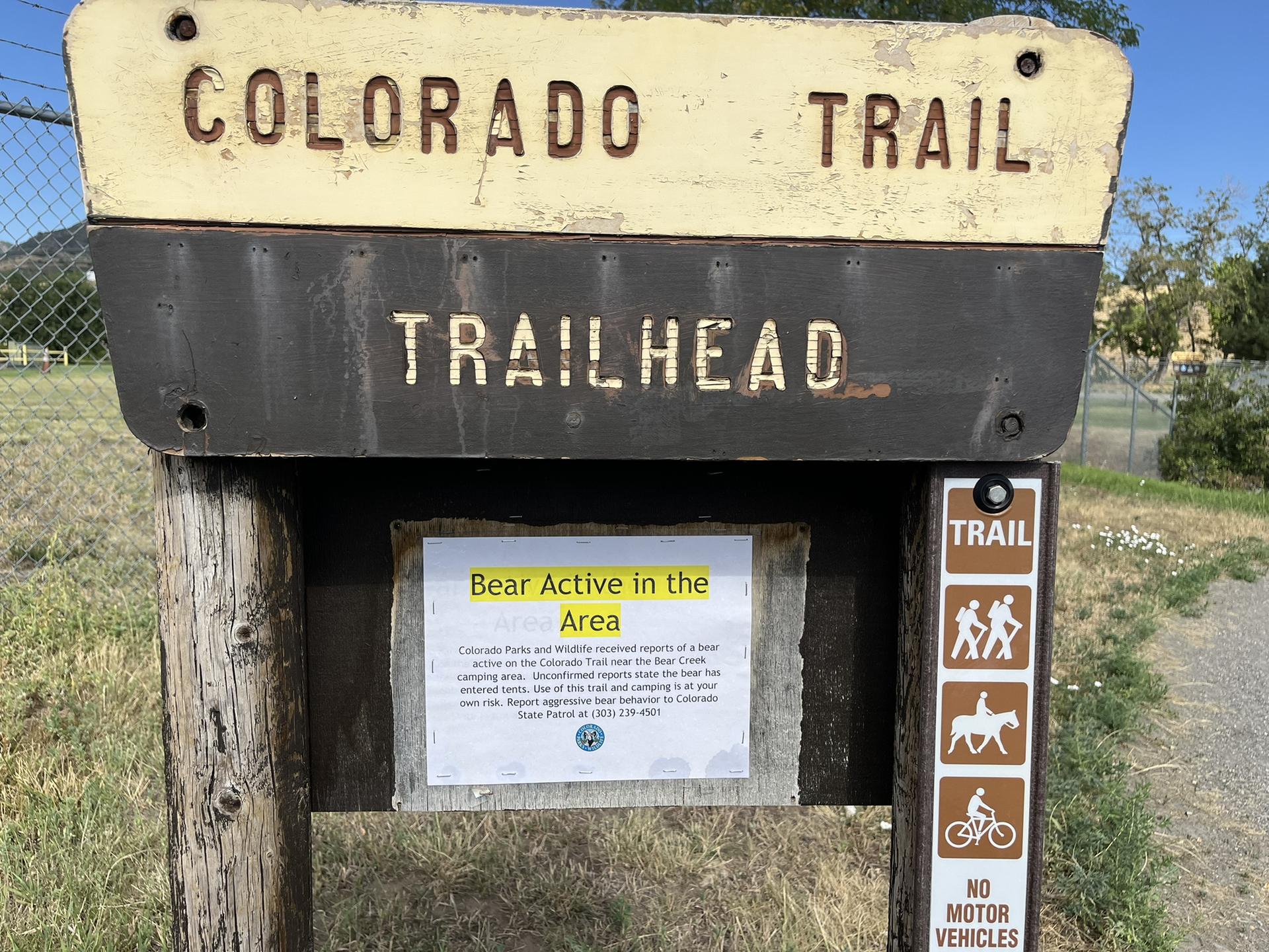 A weathered trailhead sign with a "Bear Active" warning under bright sunlight.