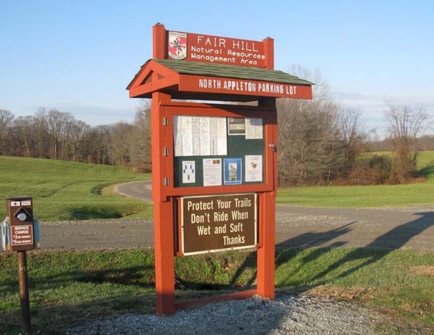 A wooden information kiosk with a brown sign in a sunny, grassy area. - Strahorn, Creek Road, and Little Egypt Loop