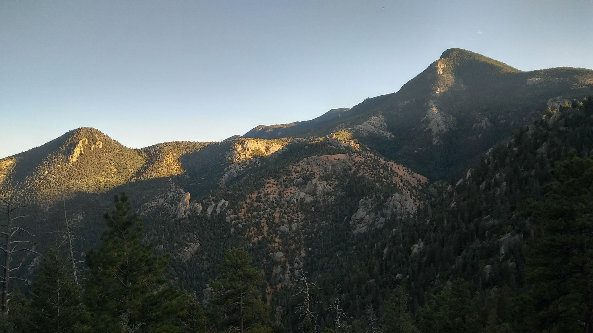 Golden light illuminates forested mountain peaks under a clear evening sky. - Manitou Incline and Barr Trail Loop