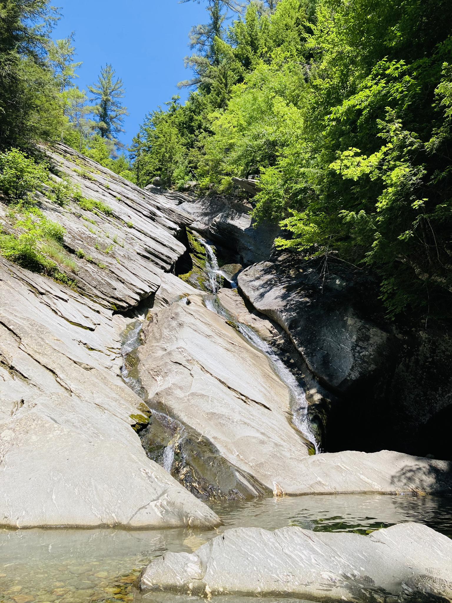 A small waterfall cascades over smooth rocks into a clear pool.