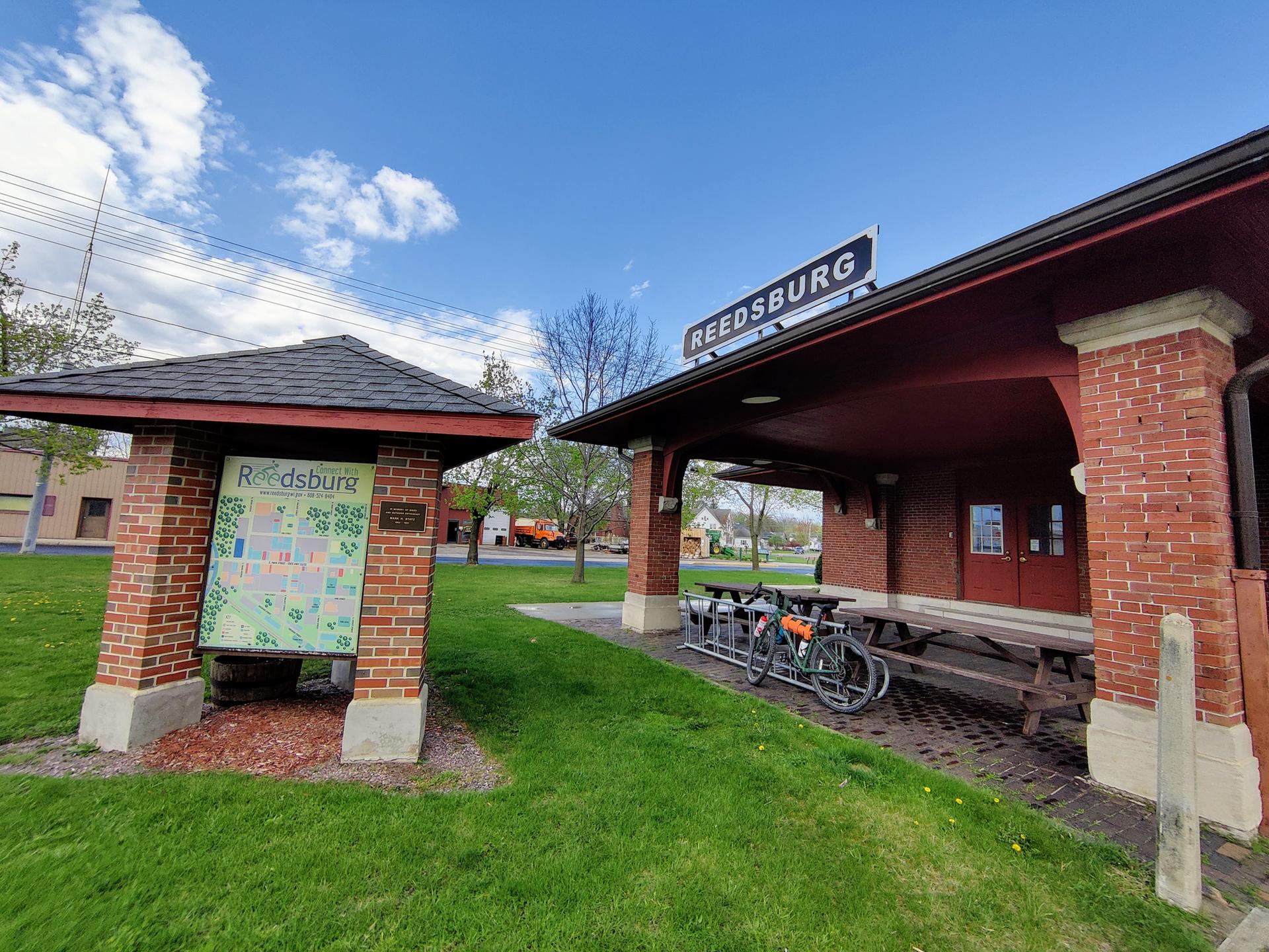 Brick building with a sign and a map kiosk on a sunny day. Two bicycles parked.