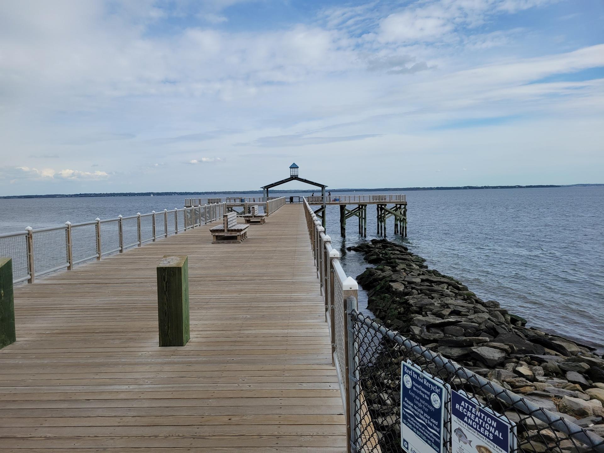 Long wooden pier extends over calm water under a cloudy sky.