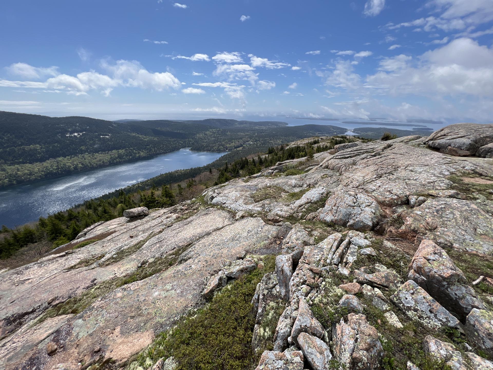 Sunny day with clouds, rocky mountain top overlooking a lake and distant ocean.
