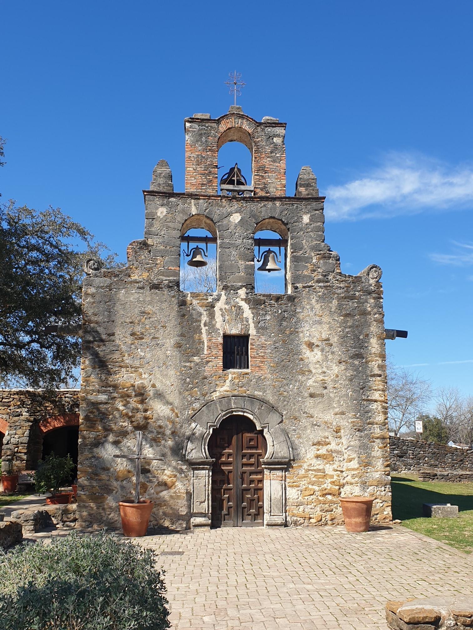 Historic stone building with bell tower under a bright blue sky.
