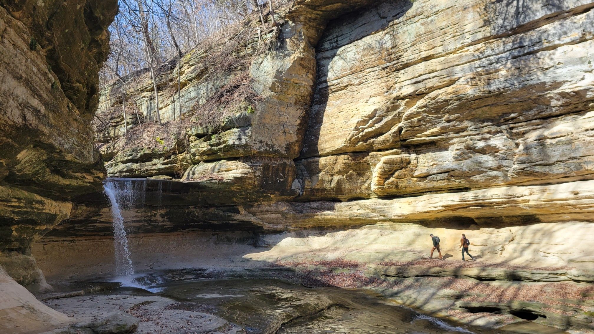 Two hikers in a sunlit canyon with a waterfall and tall rock walls. - Illinois, Kaskaskia, & La Salle Canyons