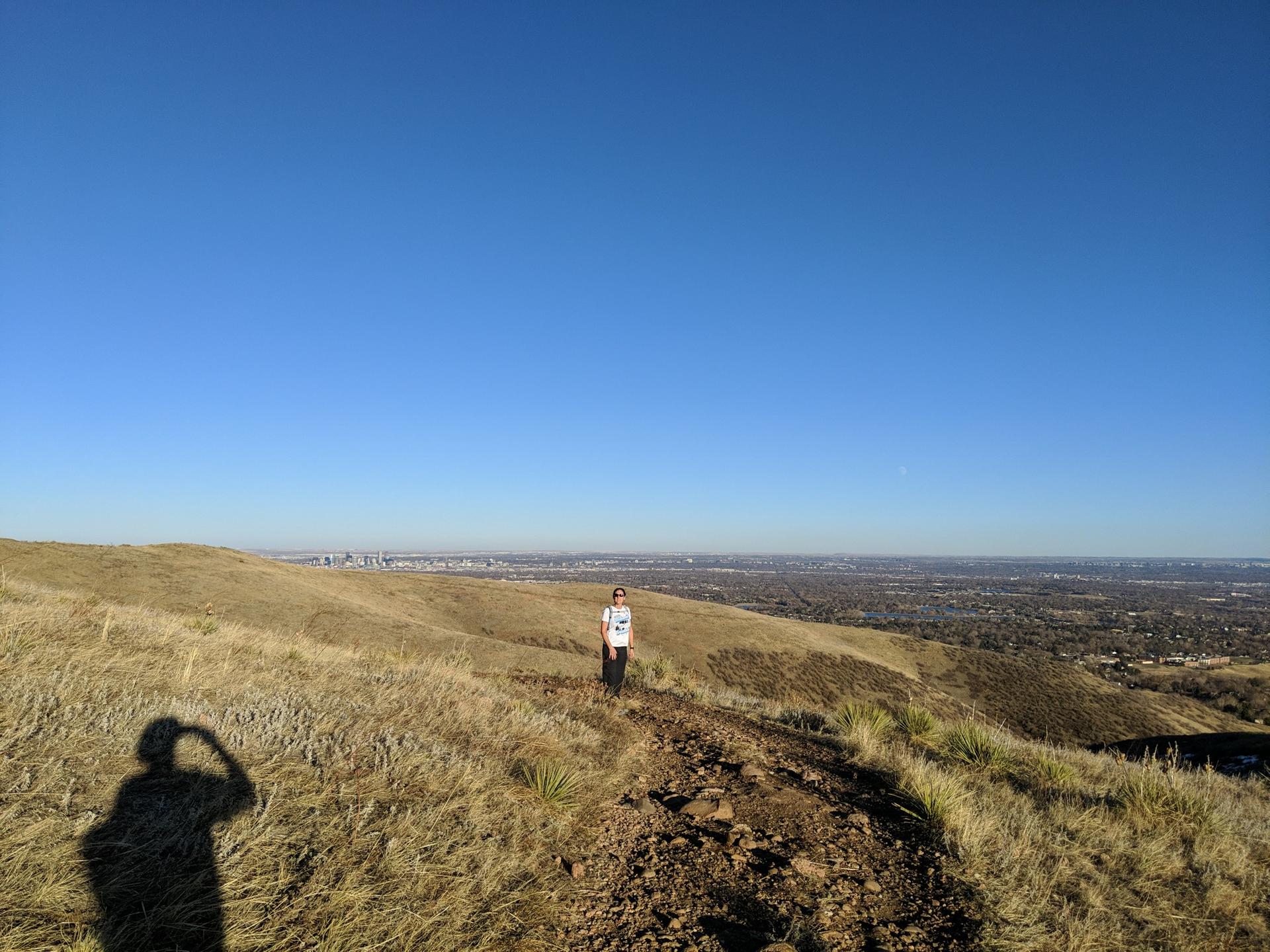 Person hiking on a sunny, dry hillside with a distant city view.