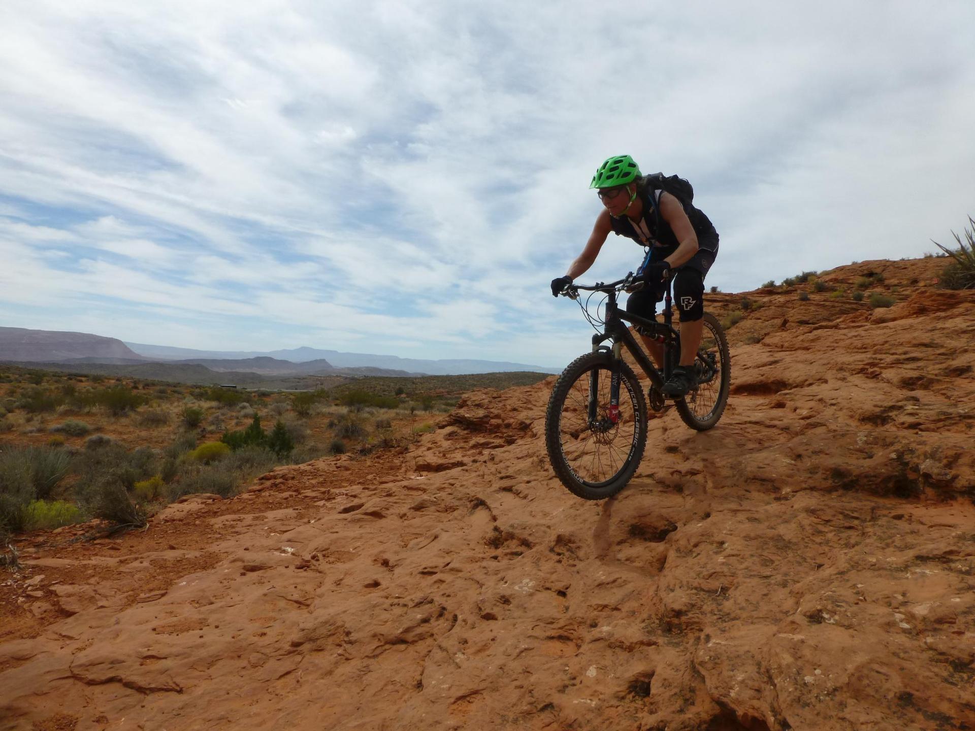 Mountain biker descends a rocky red trail under a cloudy sky.